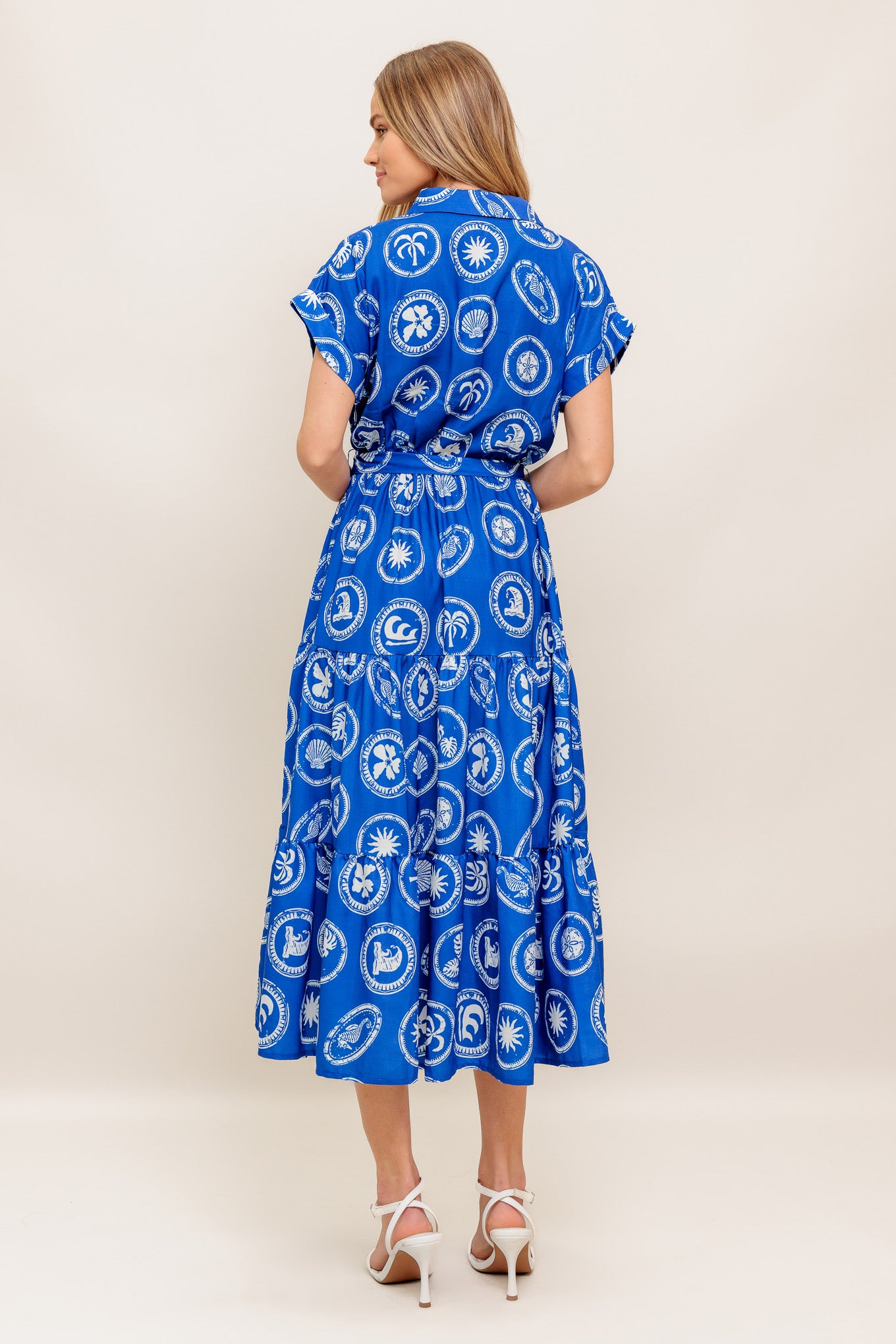 A printed woven midi dress featuring collar, surplice bodice, short cuffed sleeve, elasticized waist, self sash and tiered skirt
