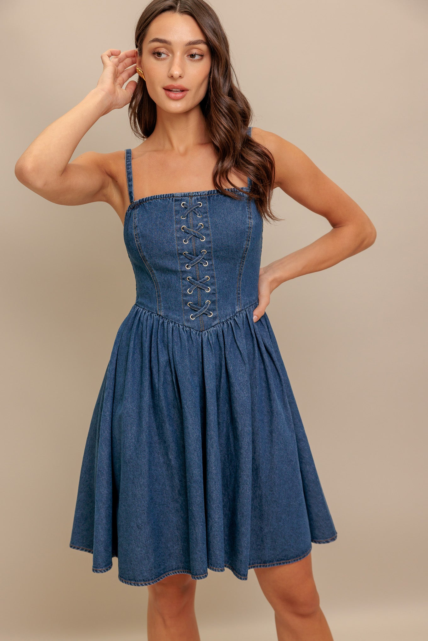 A washed denim mini dress featuring straight neckline, straps, front lace up detail, basque waistline, full skirt and smocked back bodice