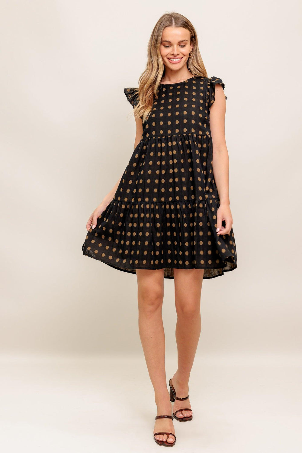 A textured woven mini dress featuring round neckline, ruffled sleeve, tiered body and back neck button closure