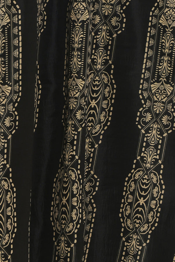 A close-up of a black fabric featuring vertical gold and beige ornate floral and geometric patterns.