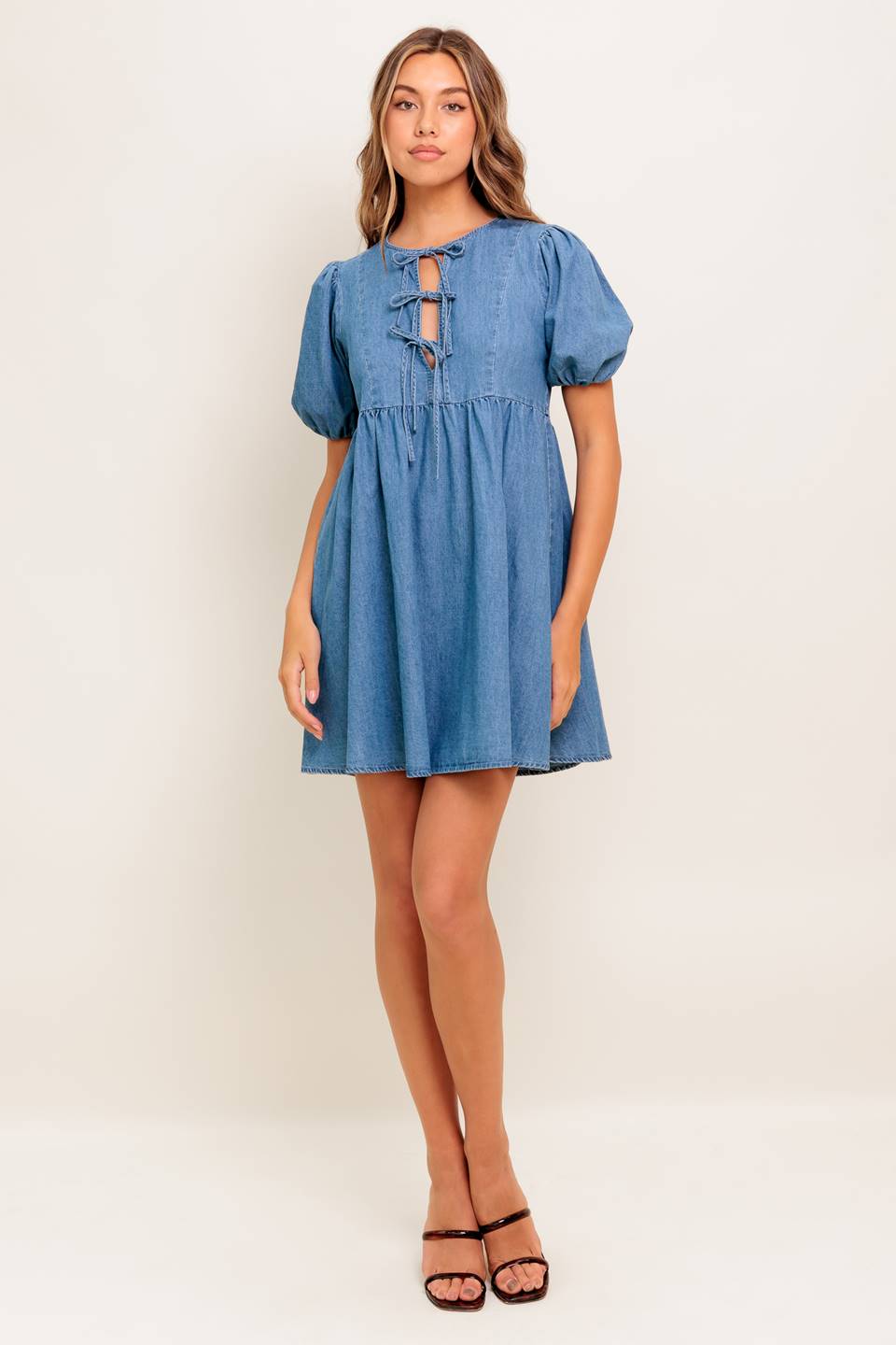 A washed denim mini dress featuring round neckline, front bow ties and short puff sleeve