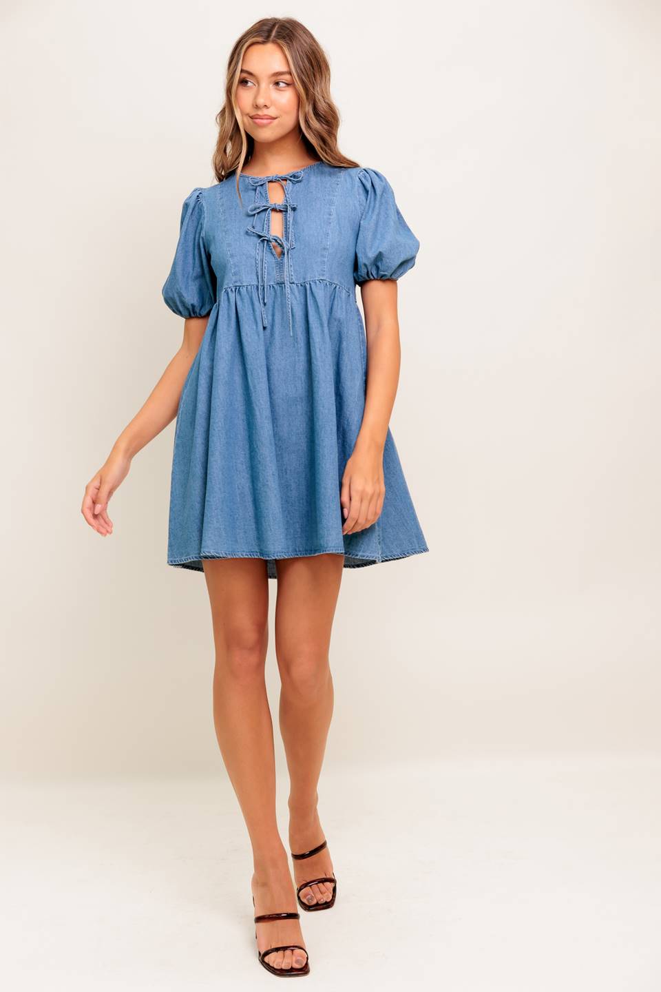 A washed denim mini dress featuring round neckline, front bow ties and short puff sleeve