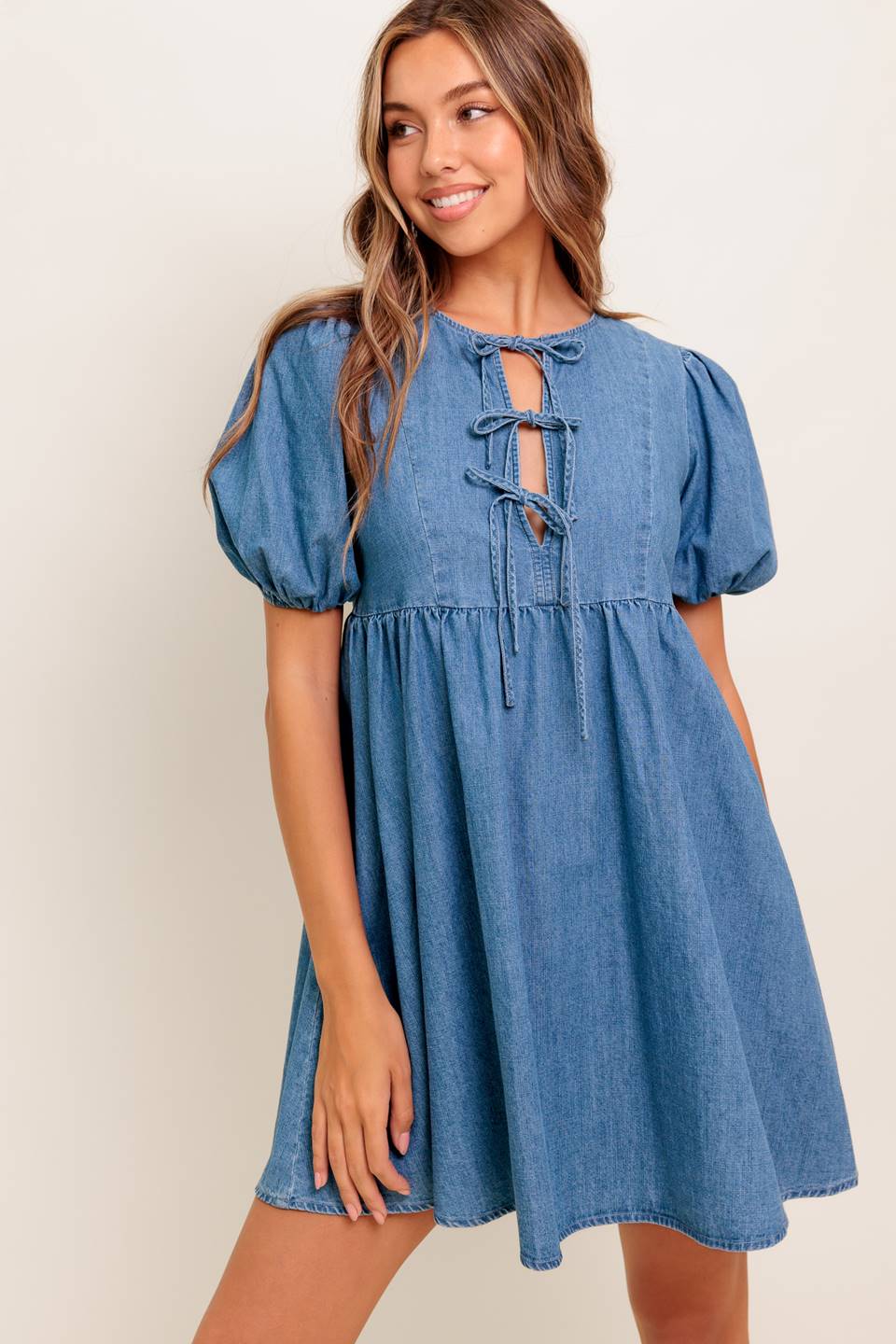 A washed denim mini dress featuring round neckline, front bow ties and short puff sleeve