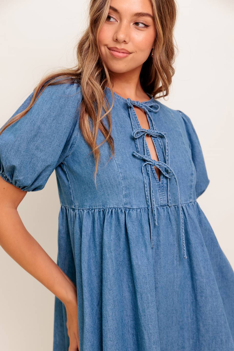A washed denim mini dress featuring round neckline, front bow ties and short puff sleeve