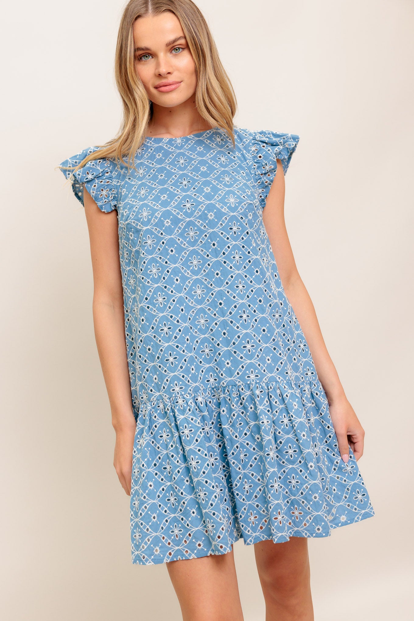 A woven eyelet babydoll dress featuring round neckline, ruffled sleeve, ruffled hemline and back tie closure