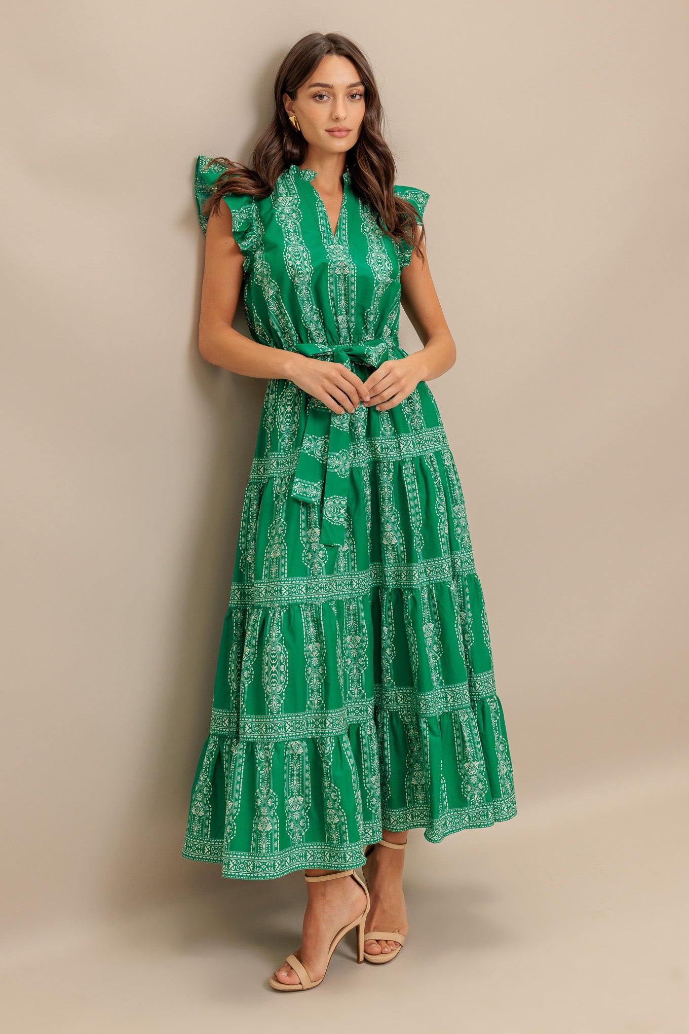 A printed woven midi dress featuring ruffled neckline with V center, short ruffle sleeve, elasticized waist with self sash tie and tiered skirt