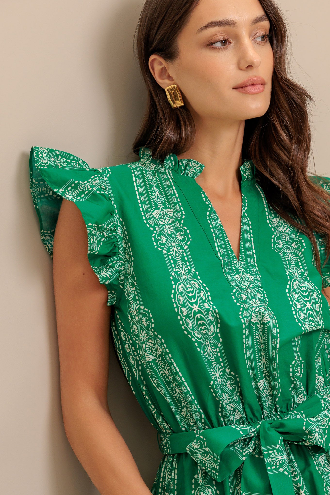 A printed woven midi dress featuring ruffled neckline with V center, short ruffle sleeve, elasticized waist with self sash tie and tiered skirt