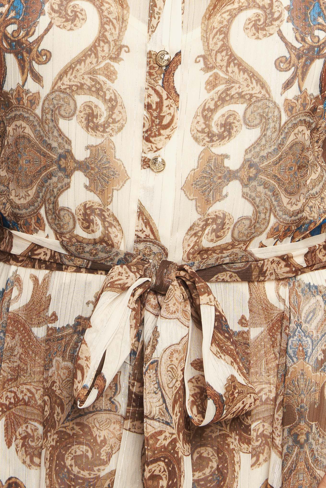 A printed woven metallic threaded maxi dress featuring collar, long sleeve with cuff, self sash tie, front button down closure and ruffled hemline