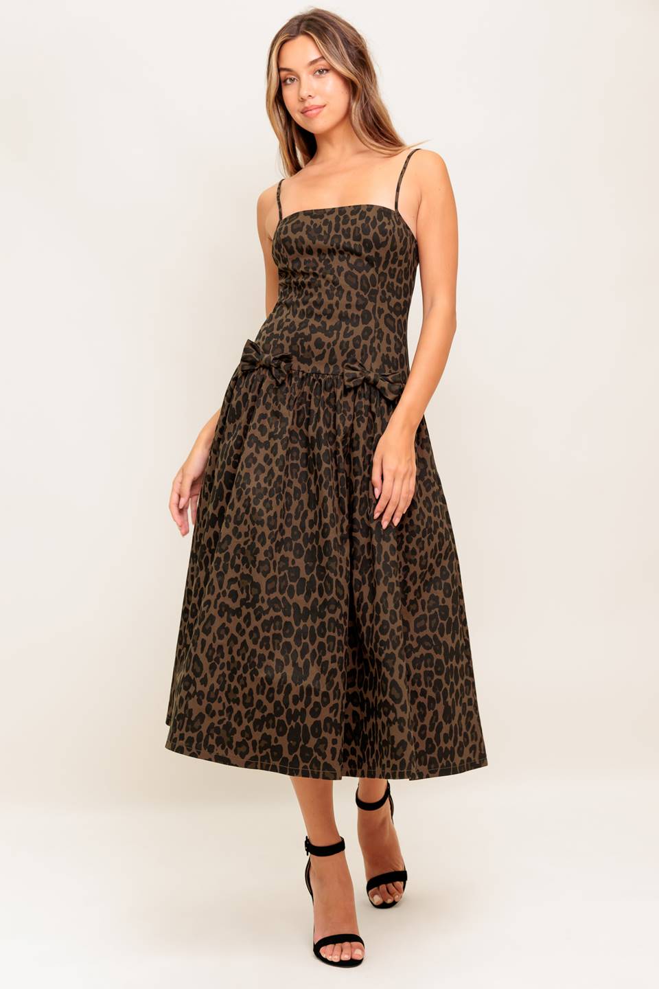 A leopard printed woven midi dress featuring straight neckline, strap, drop waist with bow detail, full skirt and back zipper closure