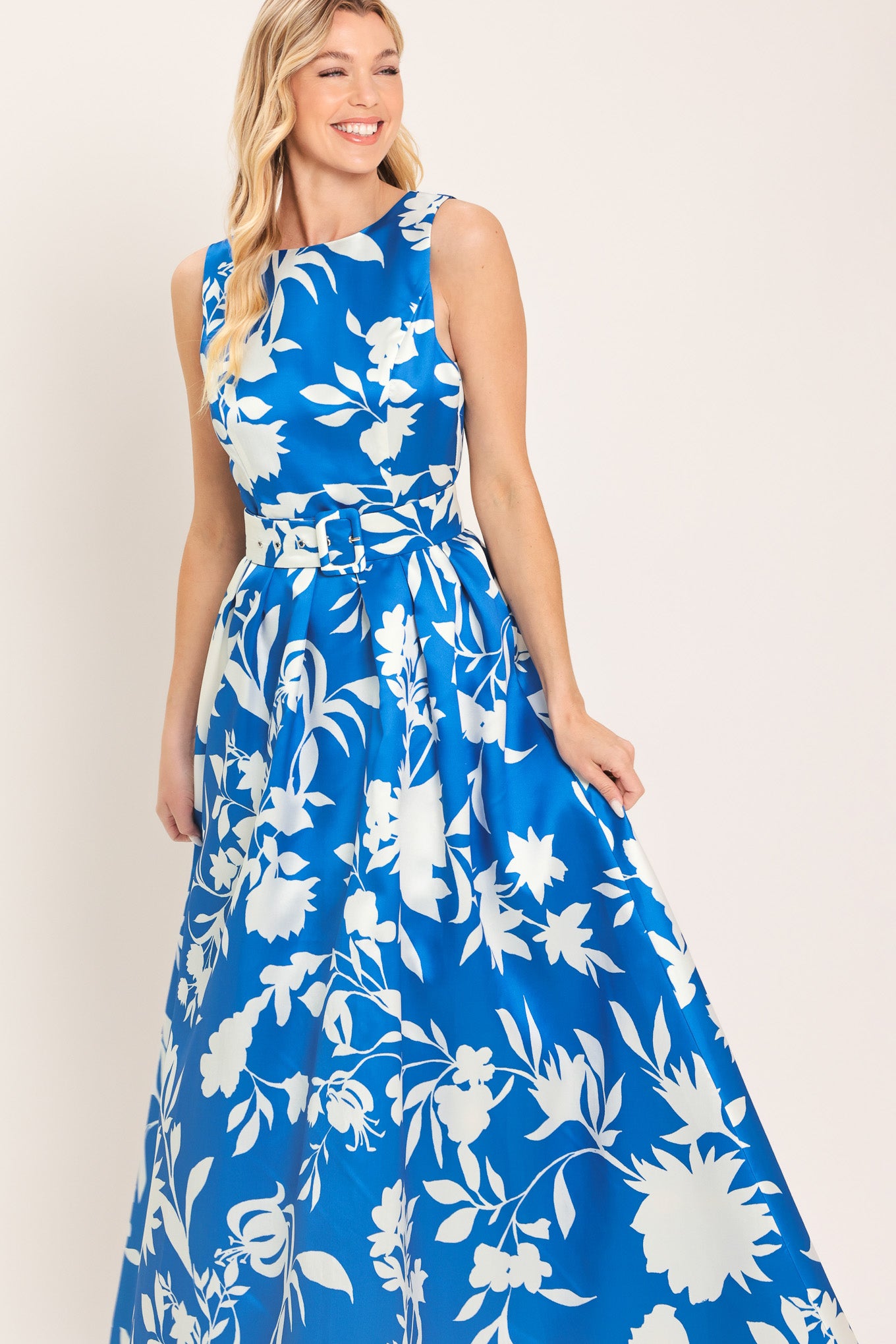 A woman wearing a sleeveless, blue maxi dress with a white floral print | Flying Tomato