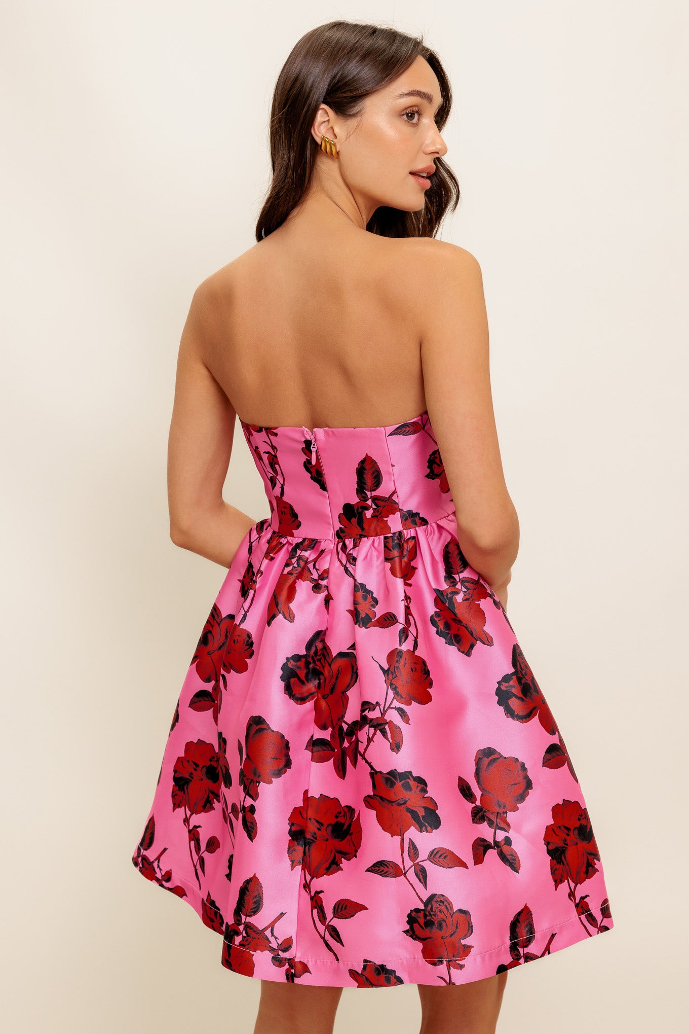 This strapless mini dress showcases a pink floral pattern on woven fabric, designed with a full skirt and secured by a back zipper closure.