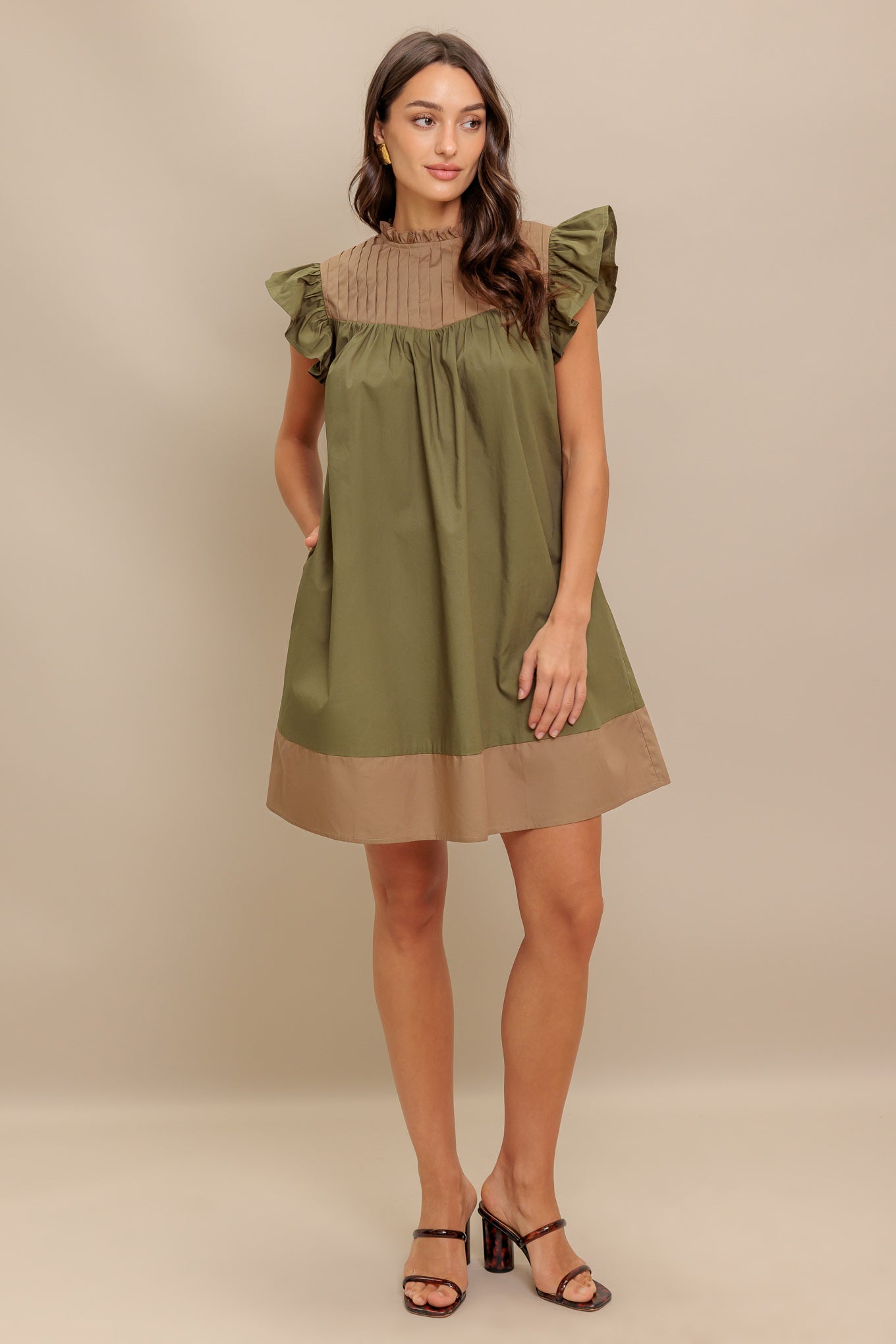 A color blocked woven mini dress featuring ruffled high neckline, ruffled short sleeve, pleated yoke and back neck button closure