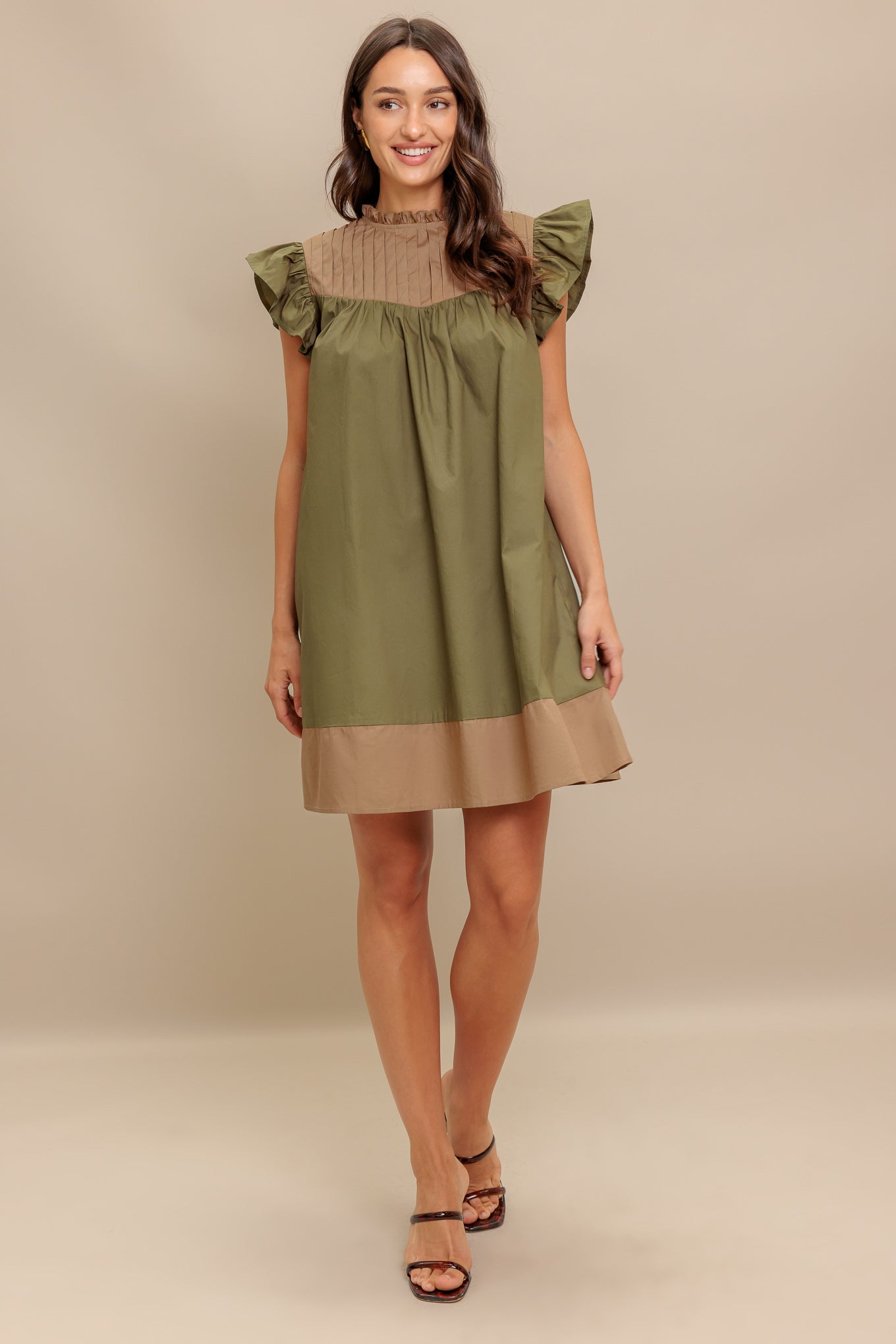 A color blocked woven mini dress featuring ruffled high neckline, ruffled short sleeve, pleated yoke and back neck button closure