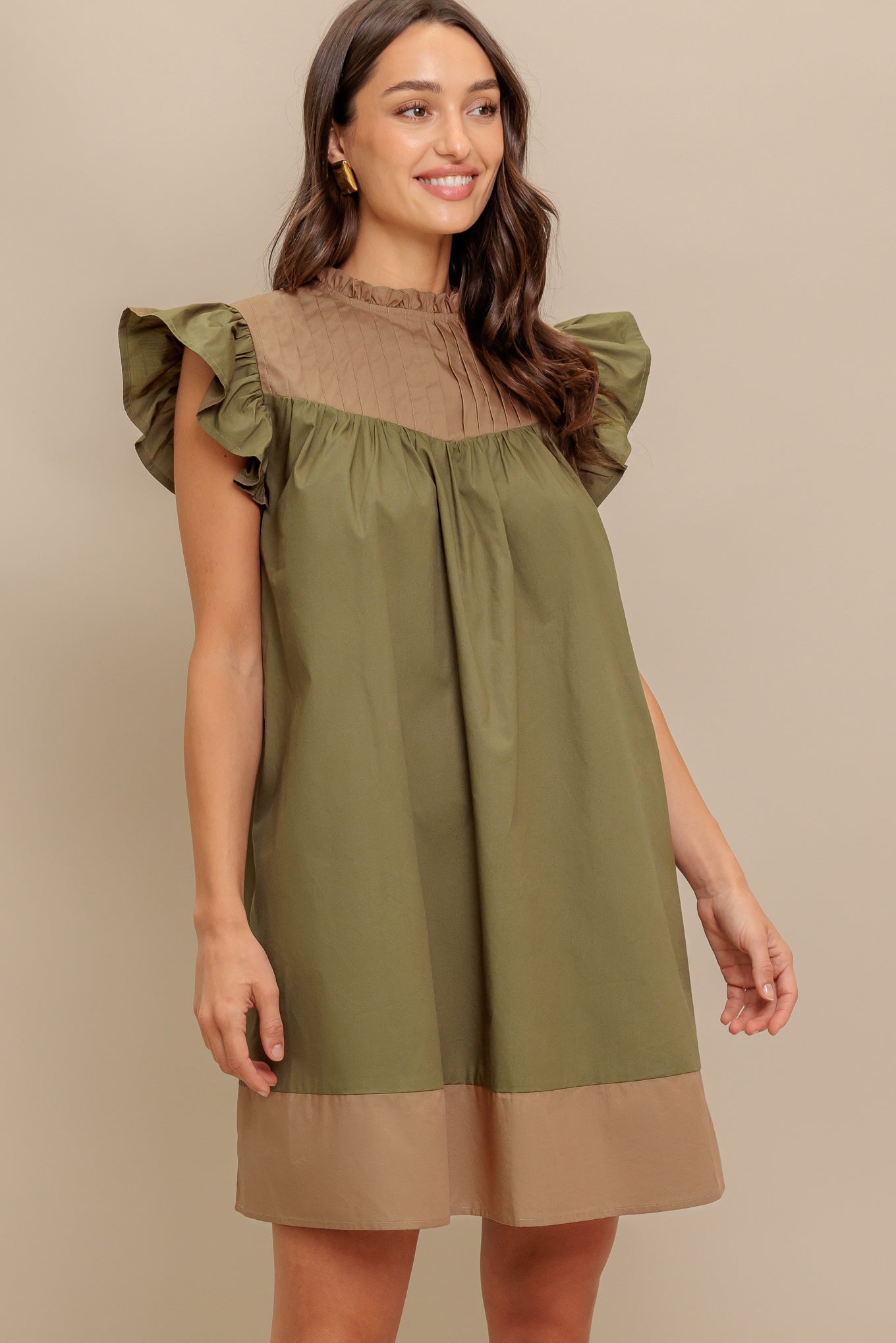 A color blocked woven mini dress featuring ruffled high neckline, ruffled short sleeve, pleated yoke and back neck button closure