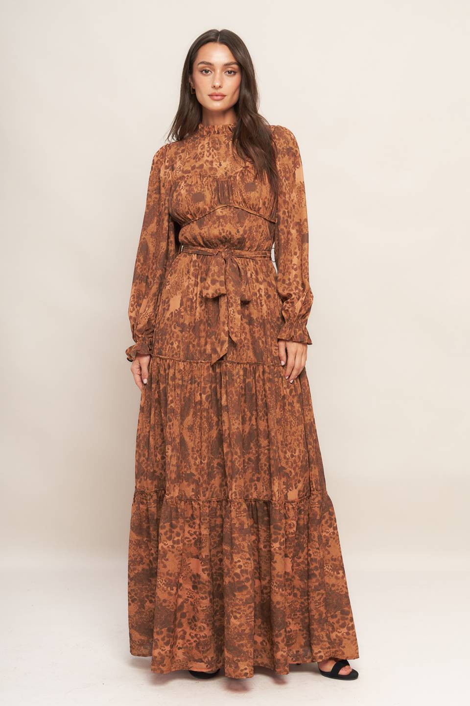 A printed woven maxi dress featuring ruffled high neckline, long sleeve, elasticized waist, self sash tie, tiered skirt and back neck button closure