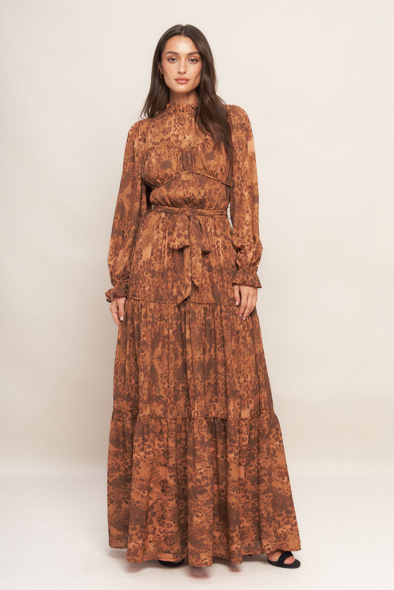 A printed woven maxi dress featuring ruffled high neckline, long sleeve, elasticized waist, self sash tie, tiered skirt and back neck button closure
