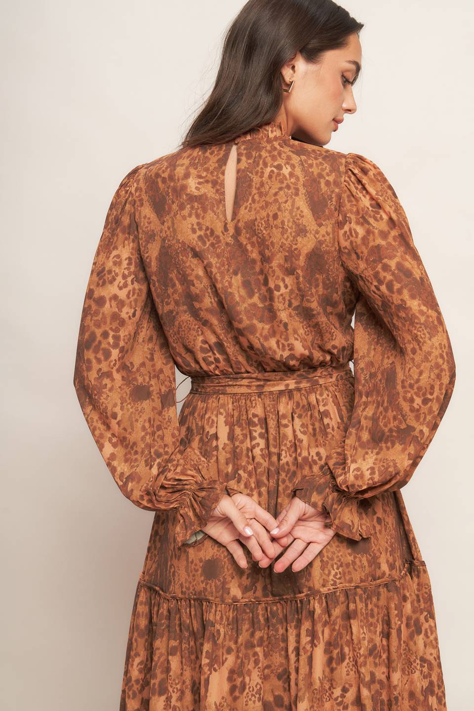 A printed woven maxi dress featuring ruffled high neckline, long sleeve, elasticized waist, self sash tie, tiered skirt and back neck button closure