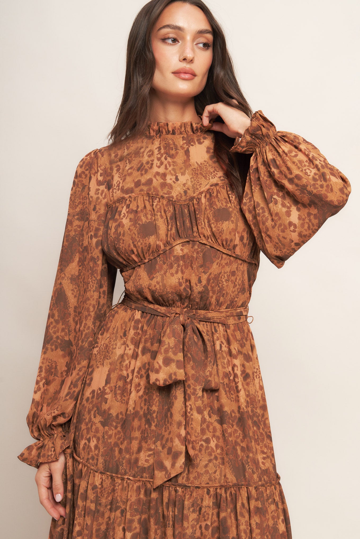 A printed woven maxi dress featuring ruffled high neckline, long sleeve, elasticized waist, self sash tie, tiered skirt and back neck button closure