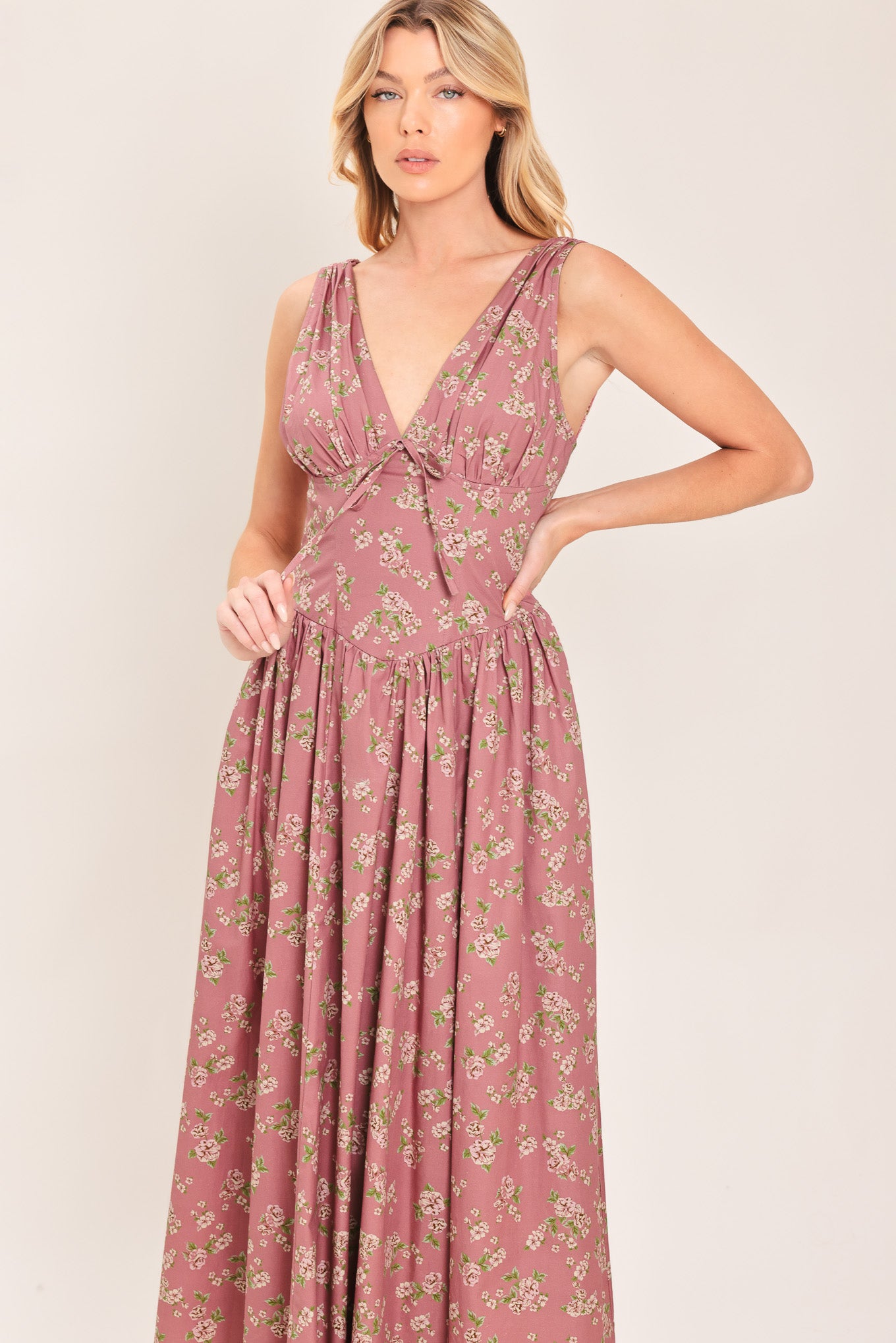 Woman wearing a mauve pink midi dress with small floral print and a woven featuring V neckline with bow tie, basque waistline, full skirt and back zipper closure | Flying Tomato