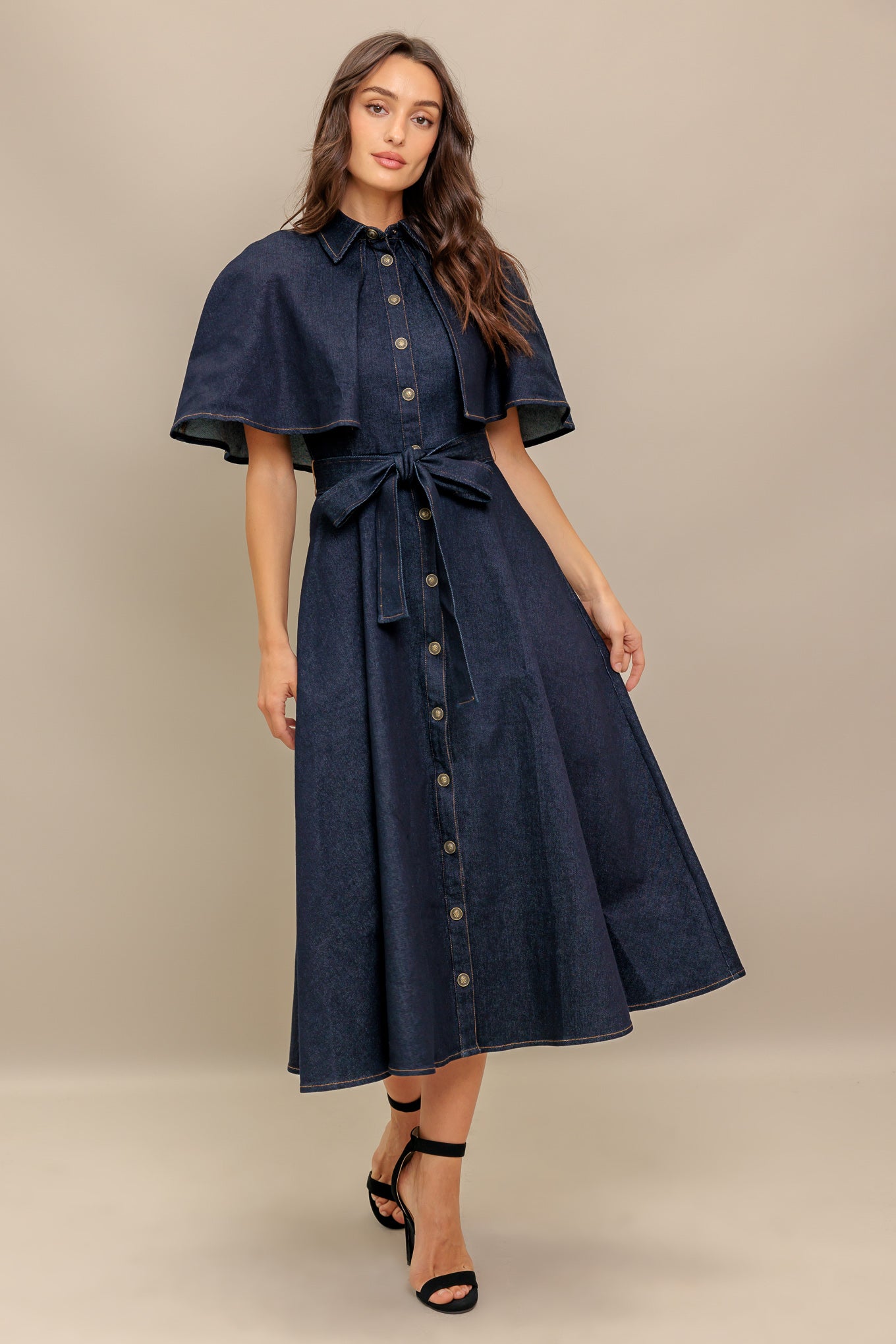 A denim midi dress featuring collar, front button down, cape top, self sash tie, and circle skirt