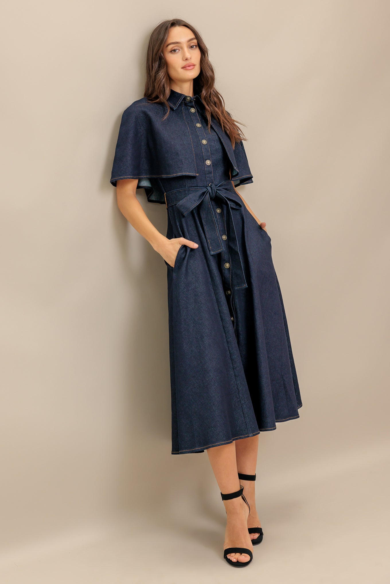 A denim midi dress featuring collar, front button down, cape top, self sash tie, and circle skirt
