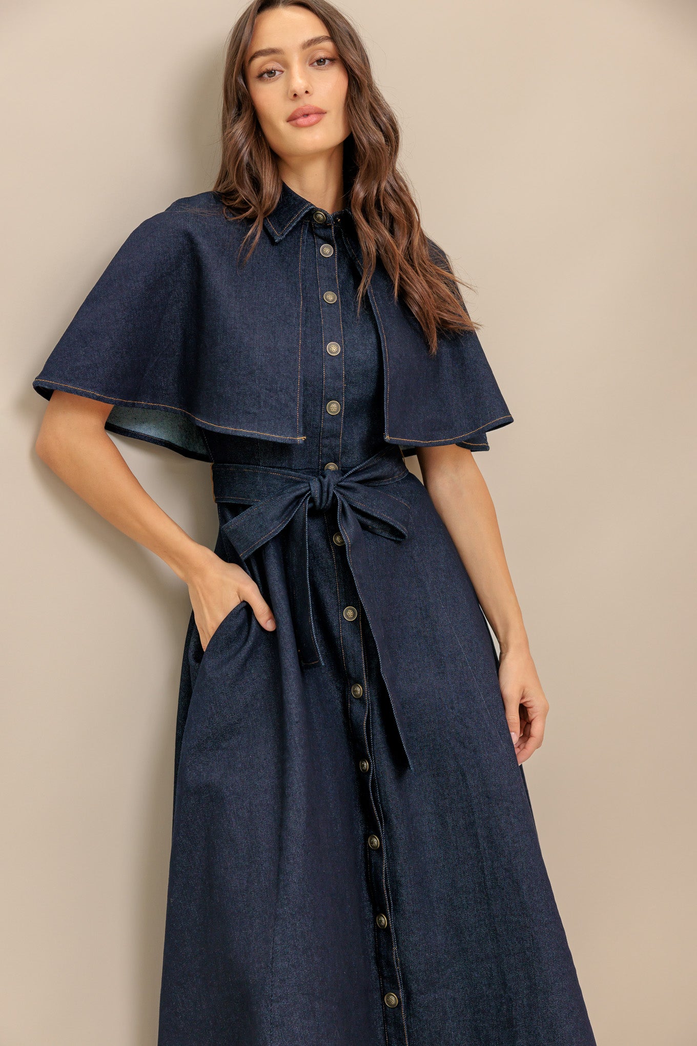 A denim midi dress featuring collar, front button down, cape top, self sash tie, and circle skirt