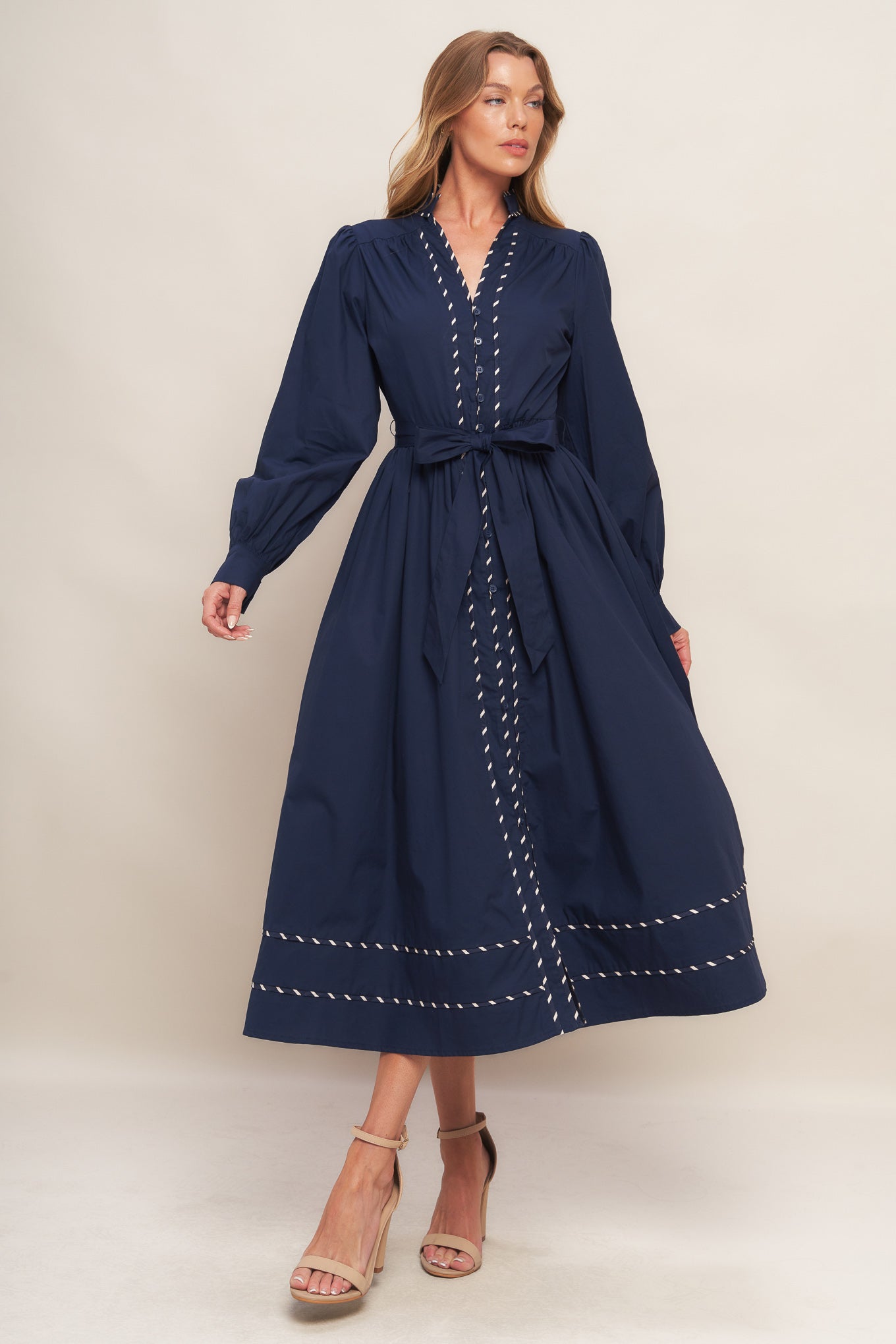 A solid woven midi dress featuring high neckline with V front, long sleeve with cuff, self sash tie, front button down and contrasting binding
