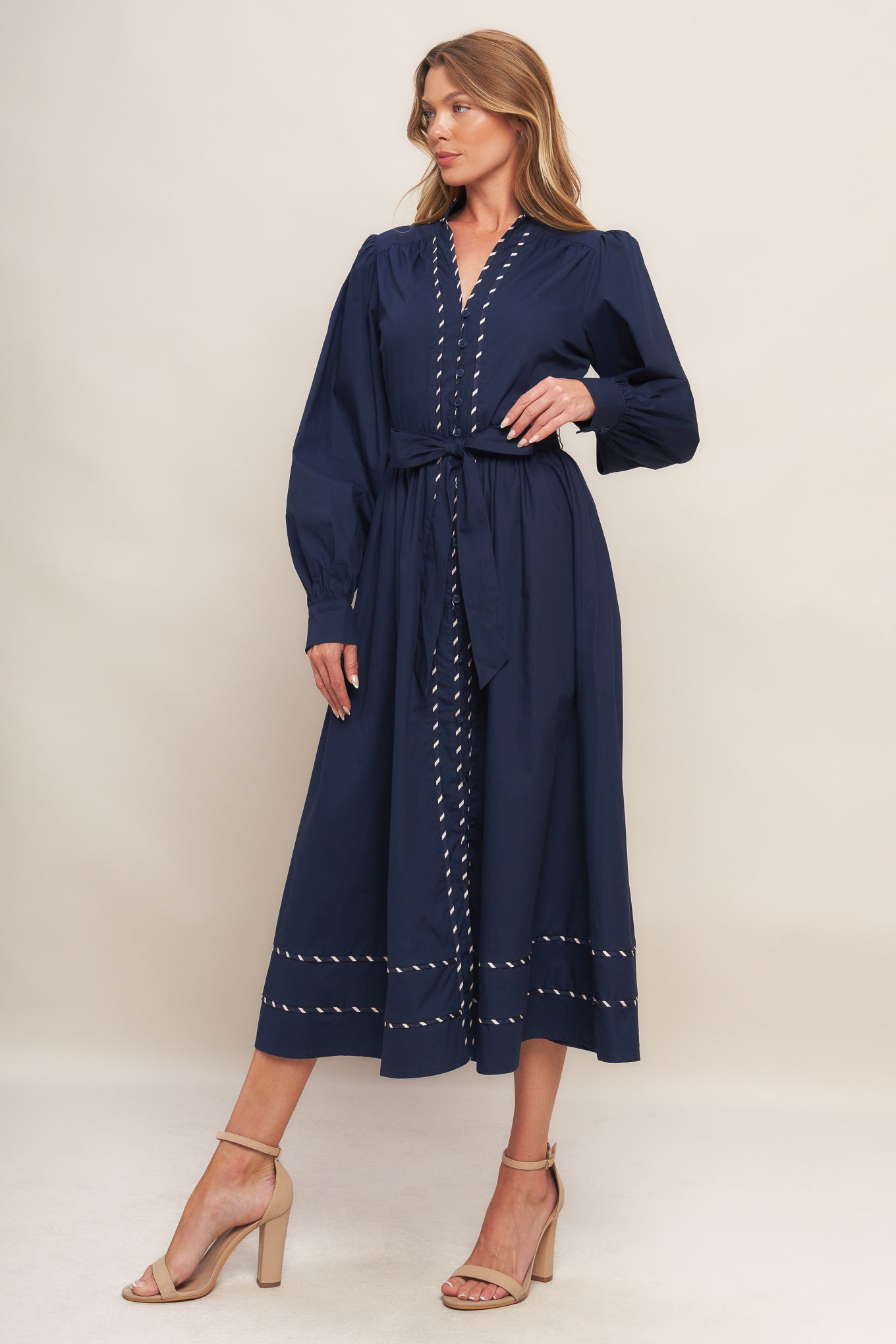 A solid woven midi dress featuring high neckline with V front, long sleeve with cuff, self sash tie, front button down and contrasting binding