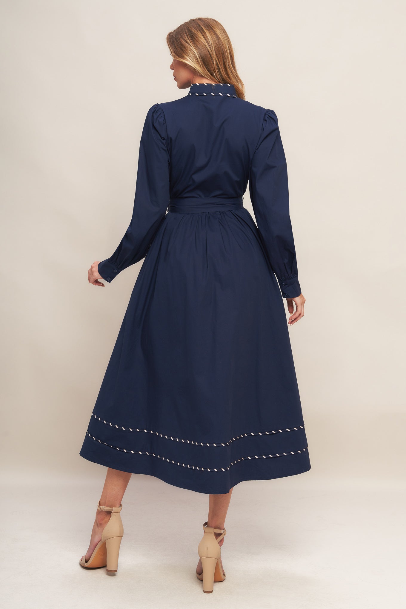 A solid woven midi dress featuring high neckline with V front, long sleeve with cuff, self sash tie, front button down and contrasting binding
