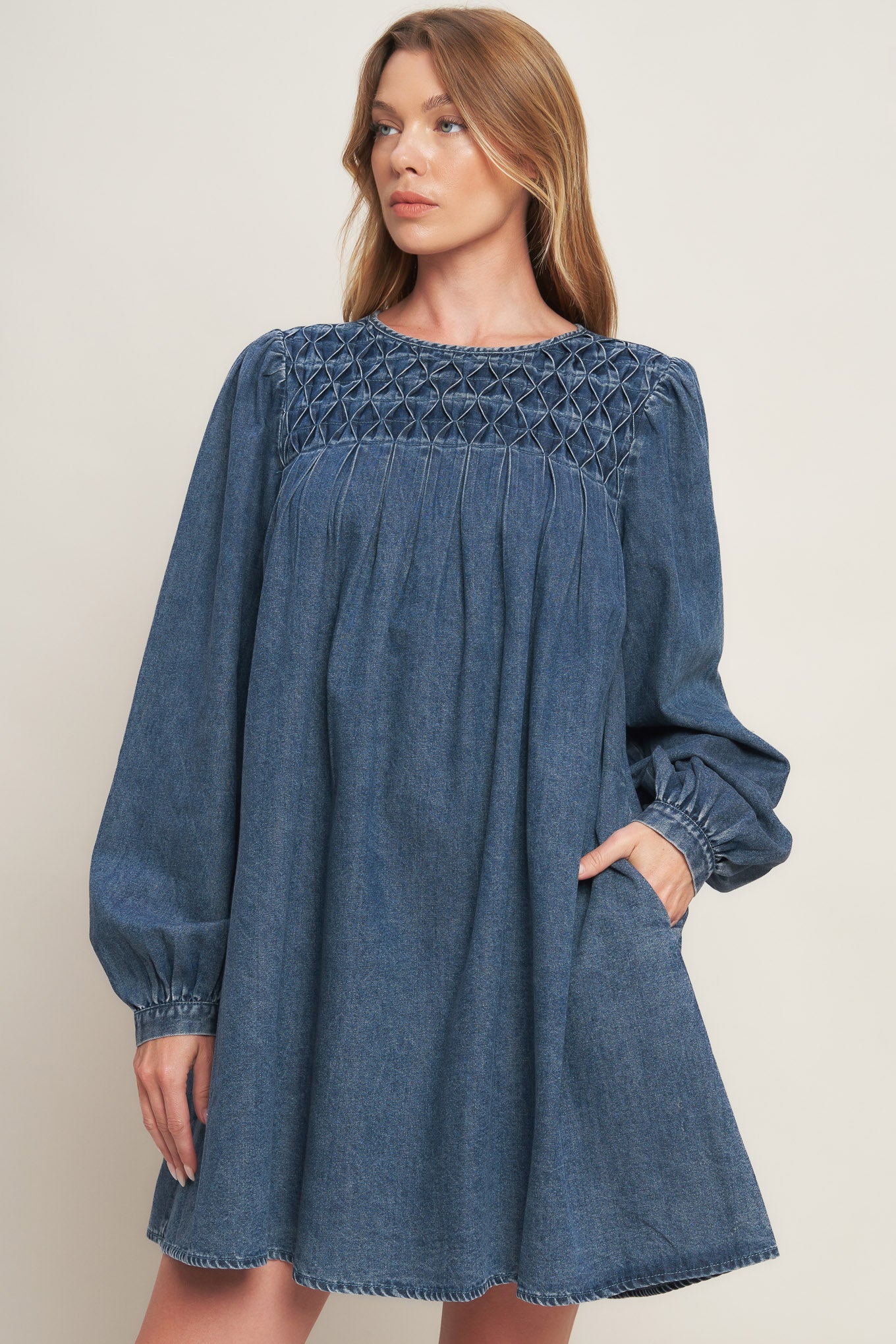 An acid washed mini dress featuring round neckline, honeycomb smocked yoke, long sleeve and back neck button closure