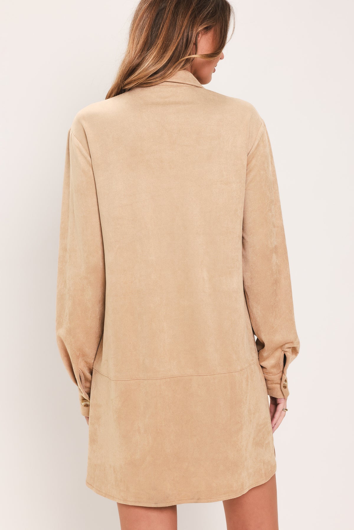 Woman wearing a long sleeve beige suede mini dress with buttons along the front, collar, and self tie matching belt | Flying Tomato