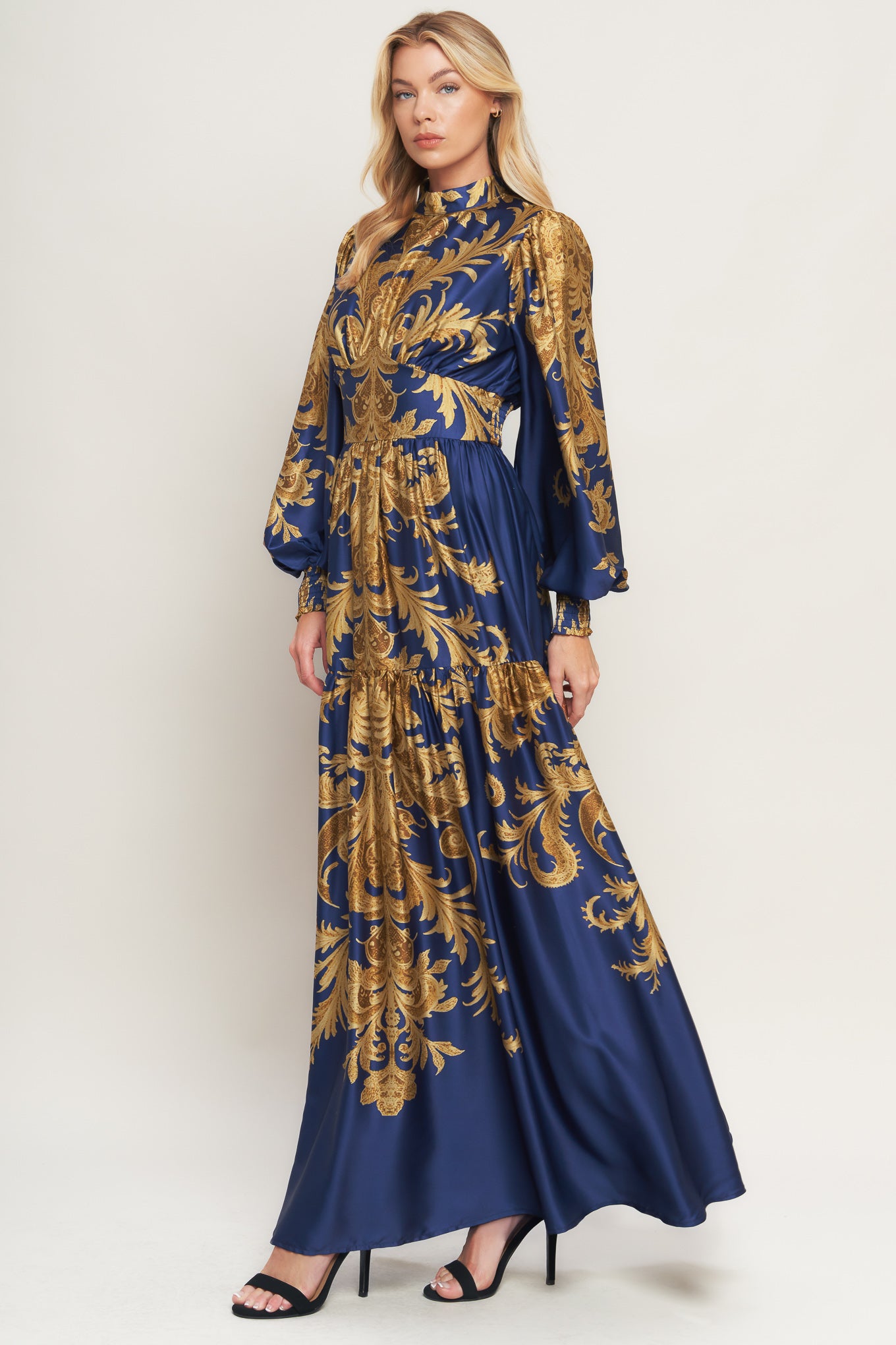 A printed woven maxi dress featuring mock neckline, blouson sleeve with smocked cuff, waist yoke, tiered skirt, smocked back waist band and back neck button closure