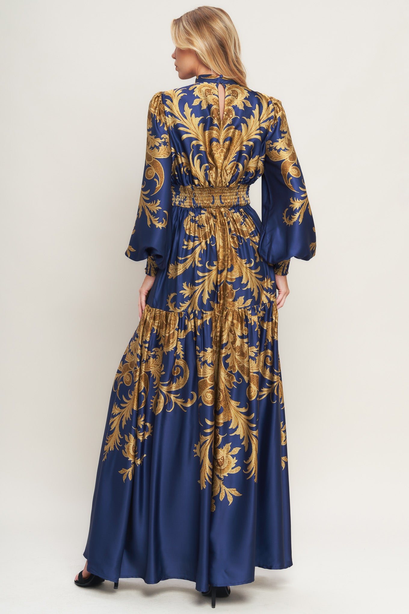 A printed woven maxi dress featuring mock neckline, blouson sleeve with smocked cuff, waist yoke, tiered skirt, smocked back waist band and back neck button closure