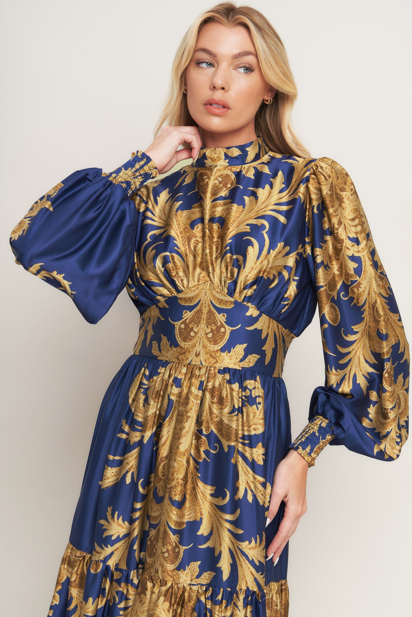 A printed woven maxi dress featuring mock neckline, blouson sleeve with smocked cuff, waist yoke, tiered skirt, smocked back waist band and back neck button closure