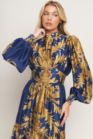 A printed woven maxi dress featuring mock neckline, blouson sleeve with smocked cuff, waist yoke, tiered skirt, smocked back waist band and back neck button closure