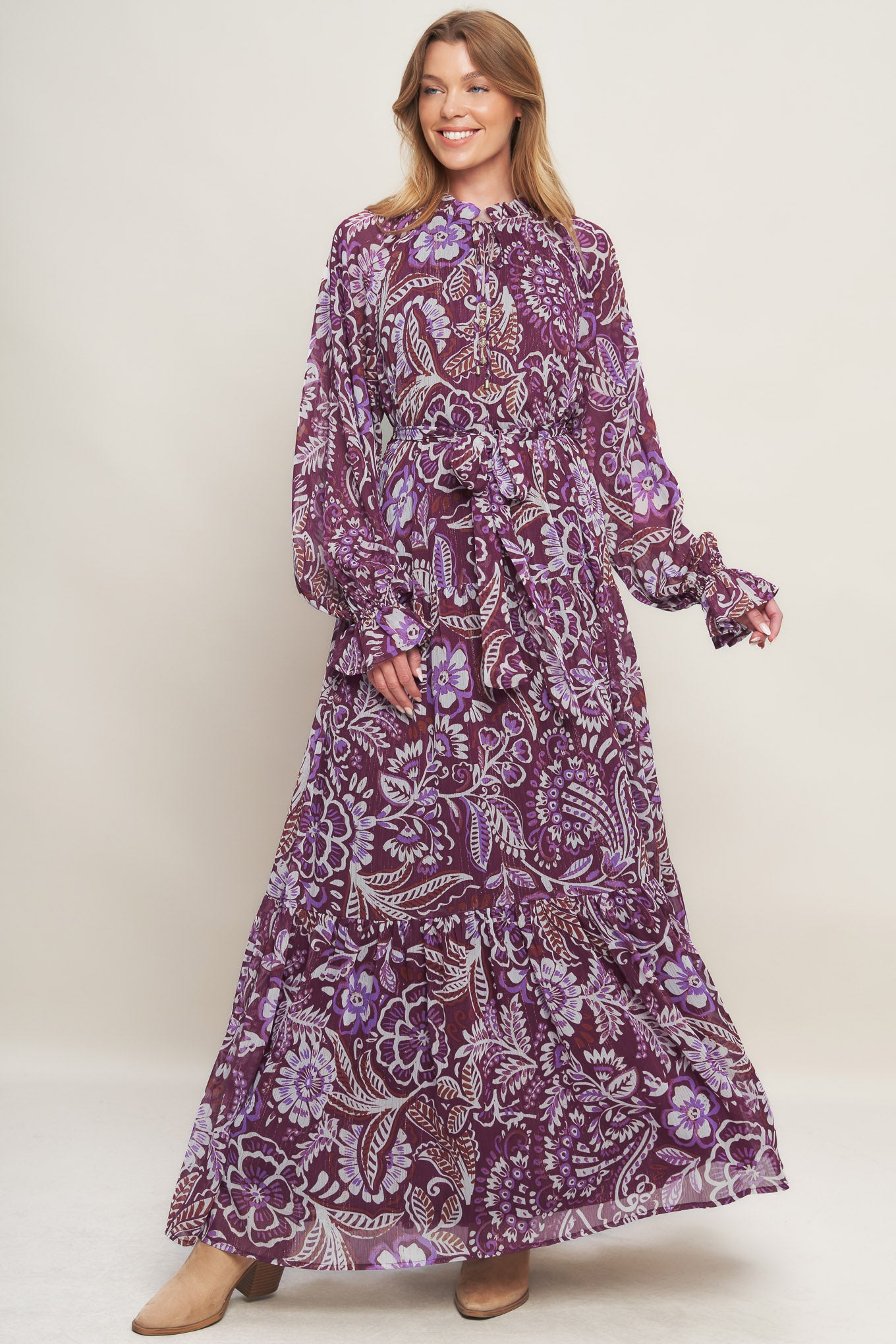 A printed woven maxi dress featuring ruffled neckline with front tie, long sleeve with ruffled cuff, tiered skirt and self sash tie
