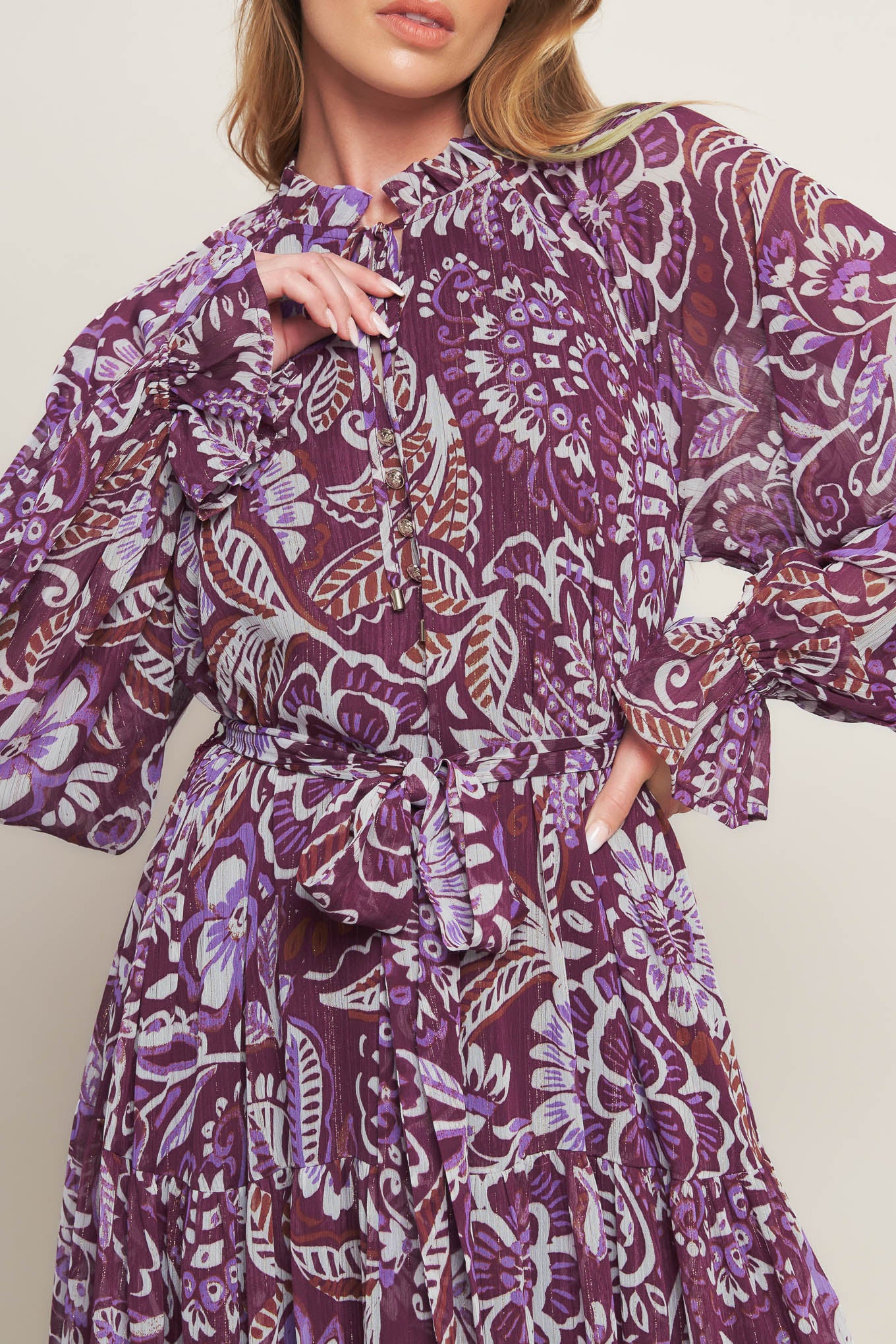 A printed woven maxi dress featuring ruffled neckline with front tie, long sleeve with ruffled cuff, tiered skirt and self sash tie