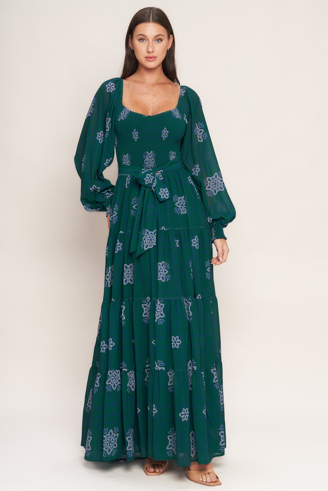 A printed woven maxi dress featuring sweetheart neckline, long sleeve with ruffled cuff, smocked bodice, tiered skirt and self sash tie