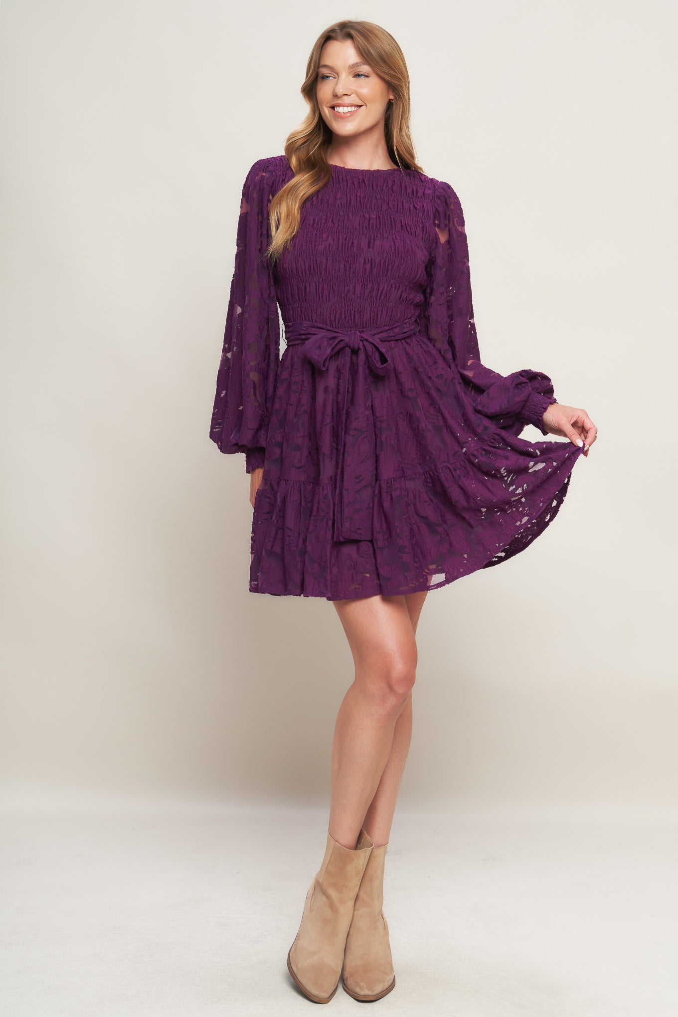 A woven lace mini dress featuring round neckline, long sleeve with cuff, smocked bodice, self sash tie, ruffled hemline and back neck button closure