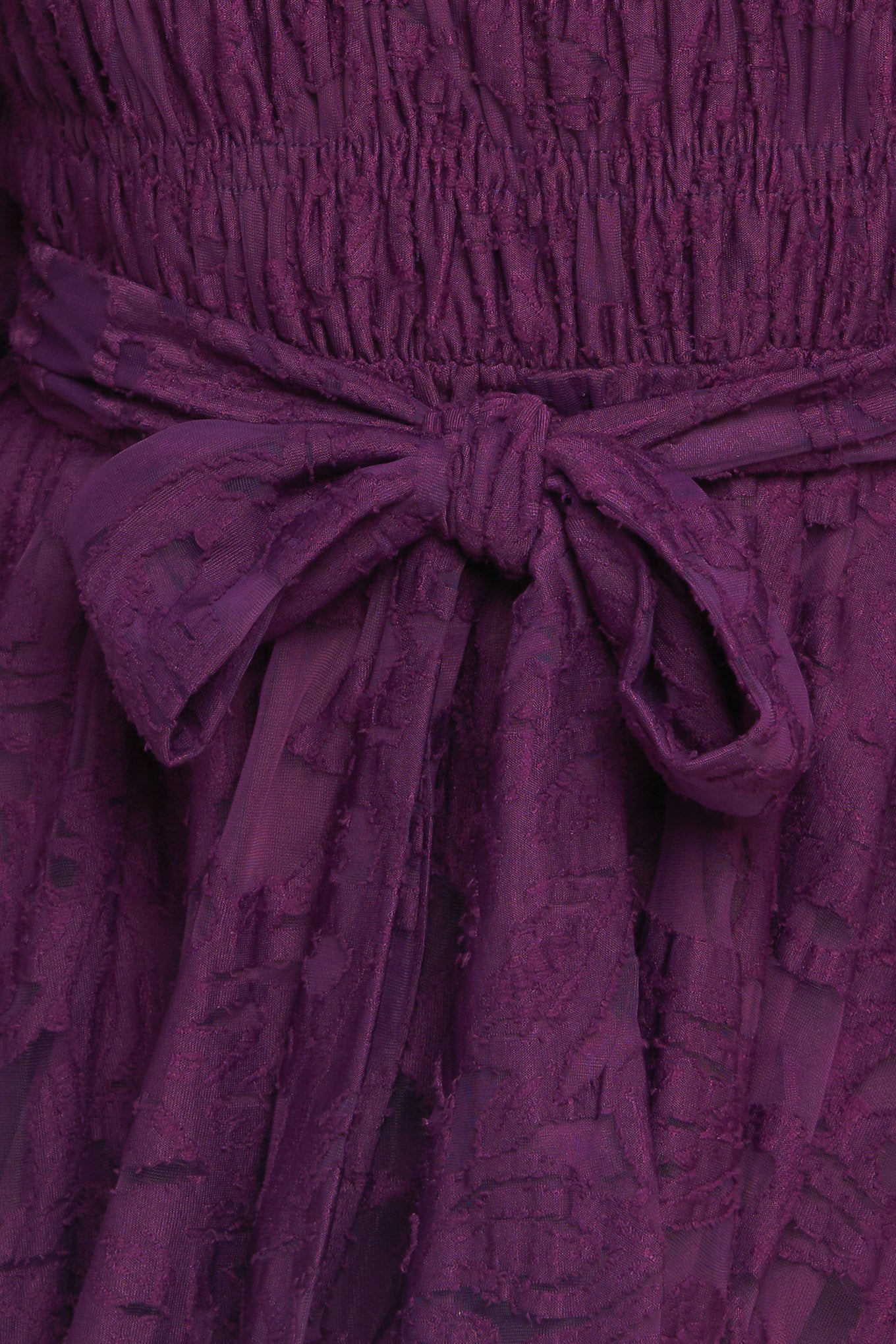A woven lace mini dress featuring round neckline, long sleeve with cuff, smocked bodice, self sash tie, ruffled hemline and back neck button closure