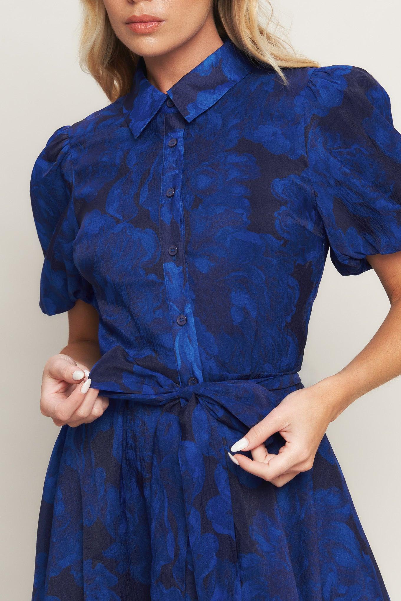 A printed woven midi dress featuring collar, front button down, short puff sleeve, self sash tie and full skirt