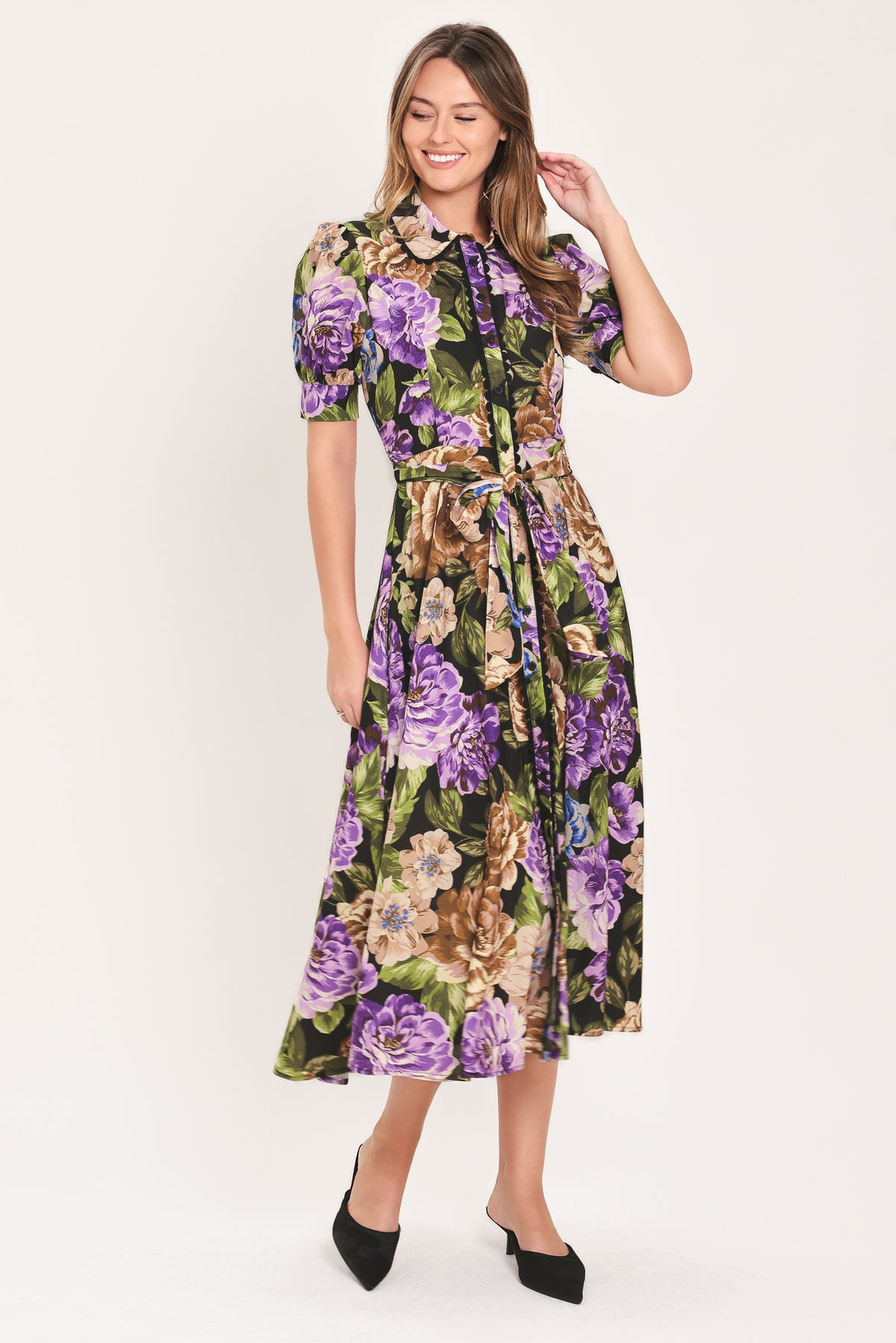 Woman wearing a black short sleeve, collared, button shirt dress with purple and gold floral pattern and a self tie waist belt | Flying Tomato