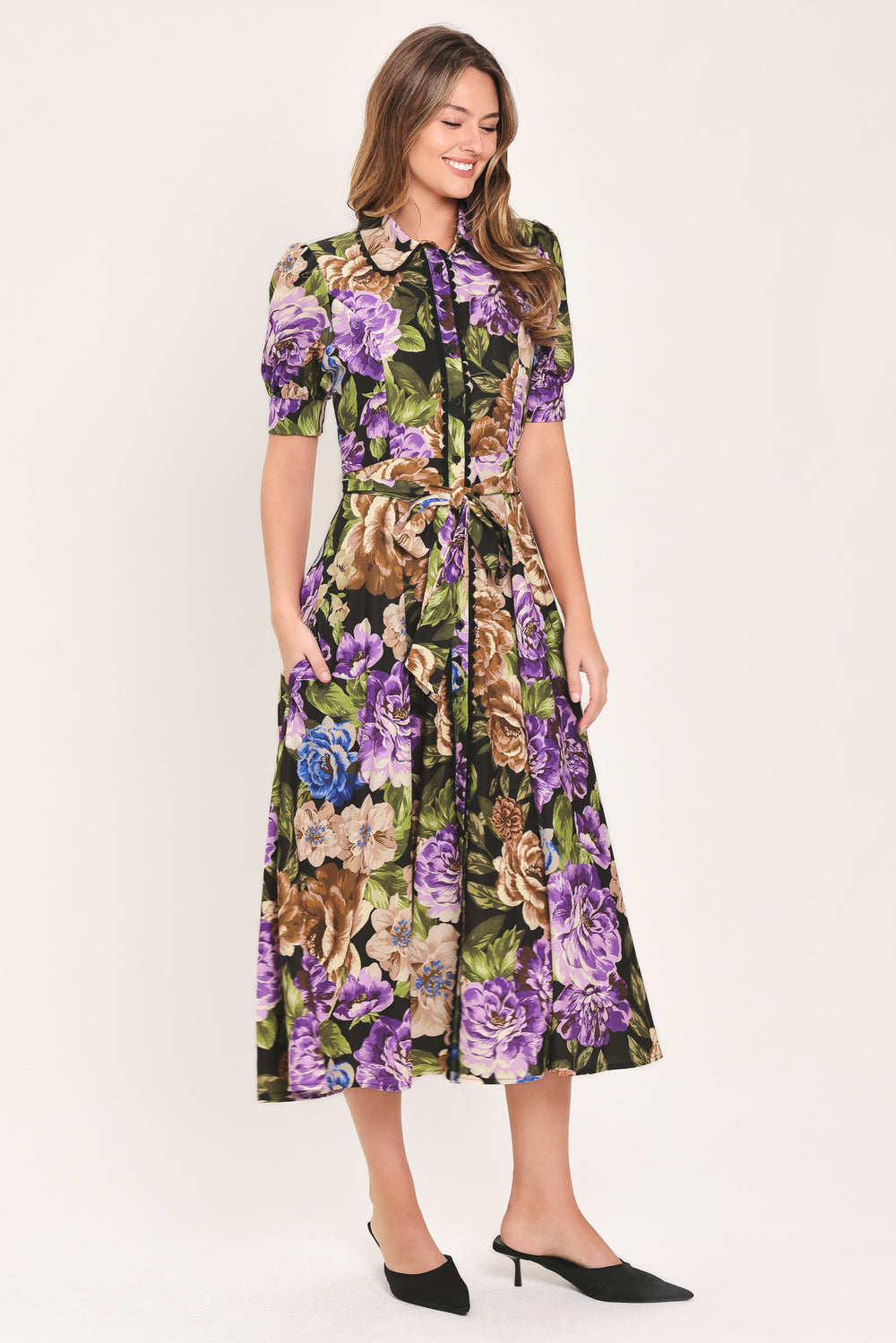 Woman wearing a black short sleeve, collared, button shirt dress with purple and gold floral pattern and a self tie waist belt | Flying Tomato