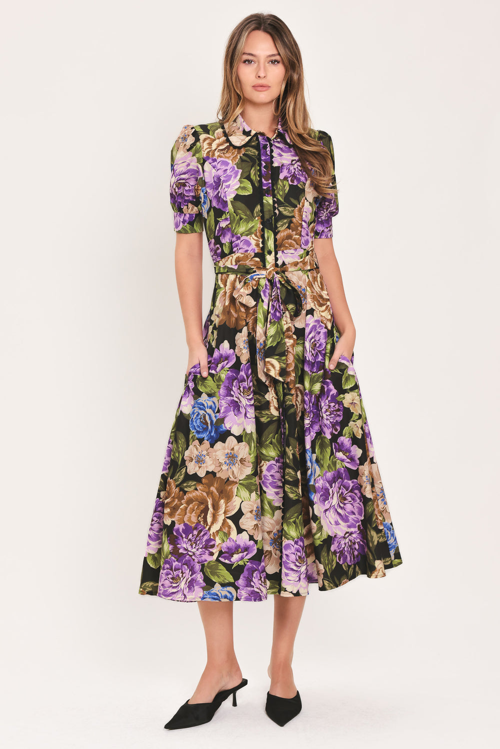Woman wearing a black short sleeve, collared, button shirt dress with purple and gold floral pattern and a self tie waist belt | Flying Tomato