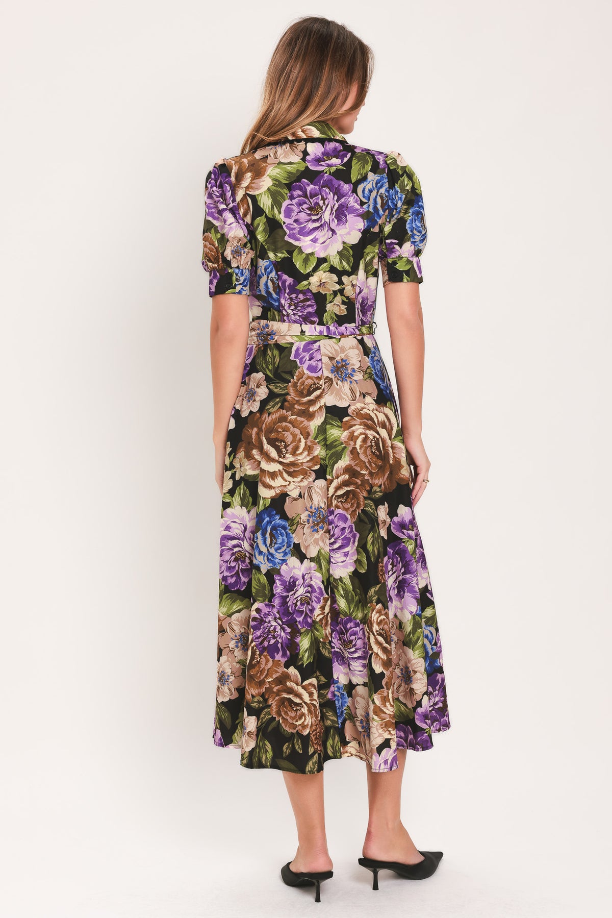 Woman wearing a black short sleeve, collared, button shirt dress with purple and gold floral pattern and a self tie waist belt | Flying Tomato