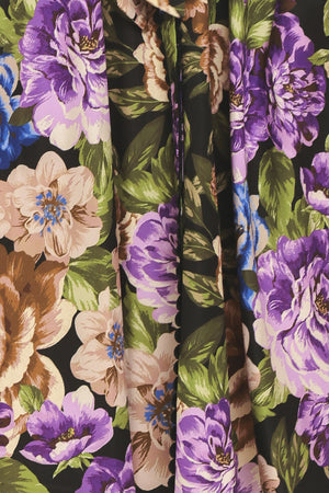 Woman wearing a black short sleeve, collared, button shirt dress with purple and gold floral pattern and a self tie waist belt | Flying Tomato