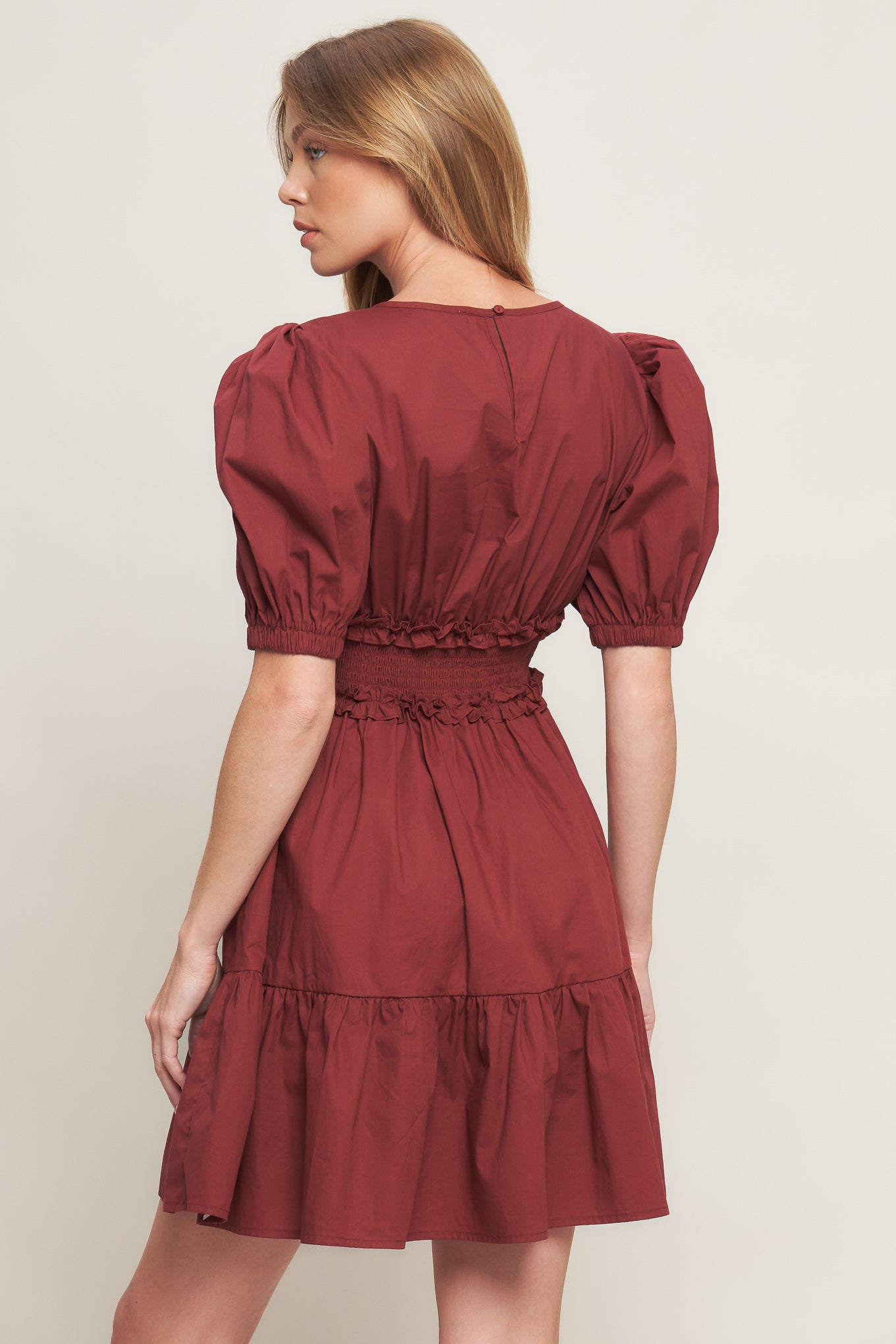 A solid woven mini dress featuring round neckline, short puff sleeve, ruffled hemline and smocked back waist band with button closure