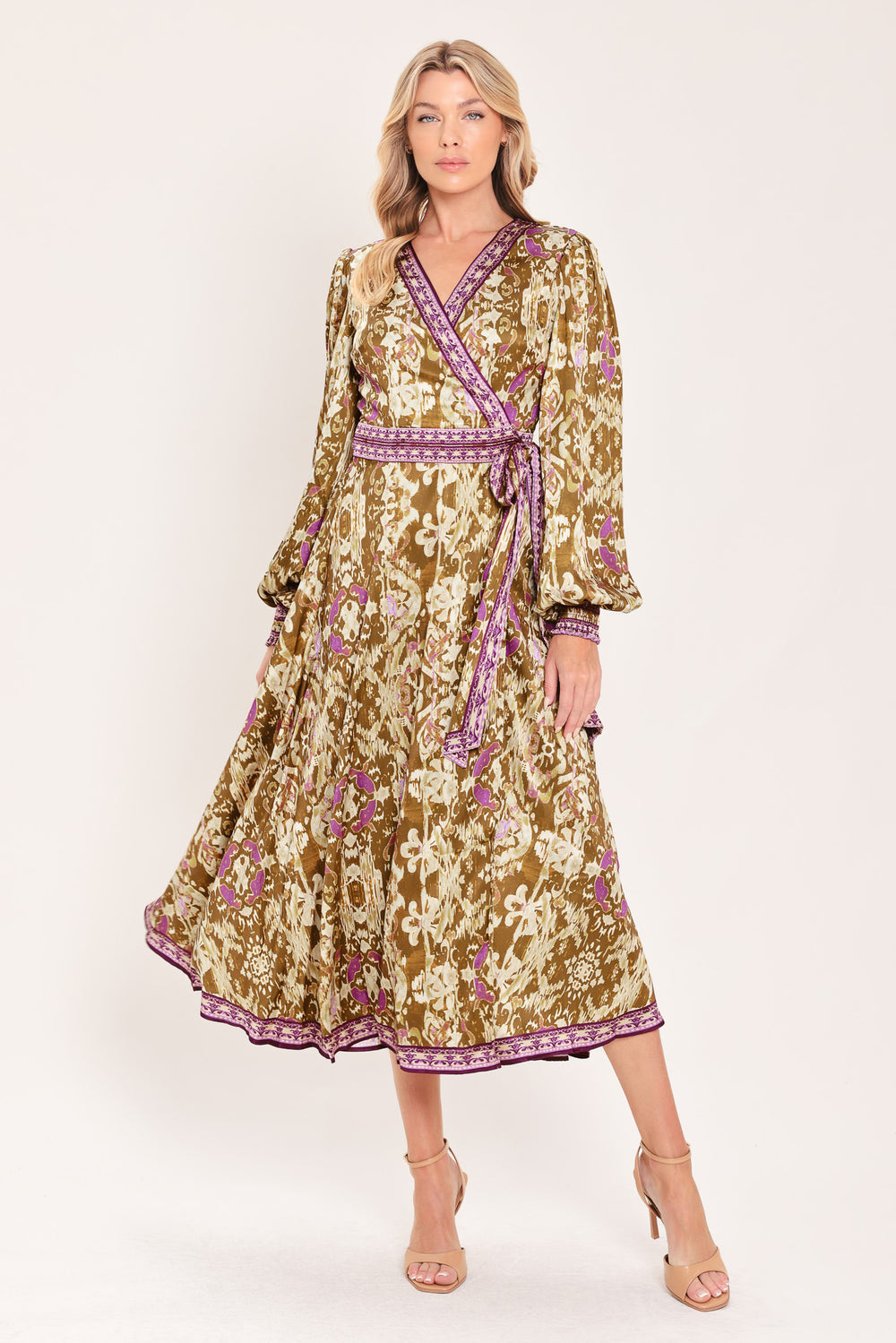A woman models a long-sleeved midi wrap dress with a brown, beige, and purple floral pattern. The dress features a matching purple patterned belt and hem | Flying Tomato