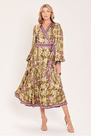 A woman models a long-sleeved midi wrap dress with a brown, beige, and purple floral pattern. The dress features a matching purple patterned belt and hem | Flying Tomato