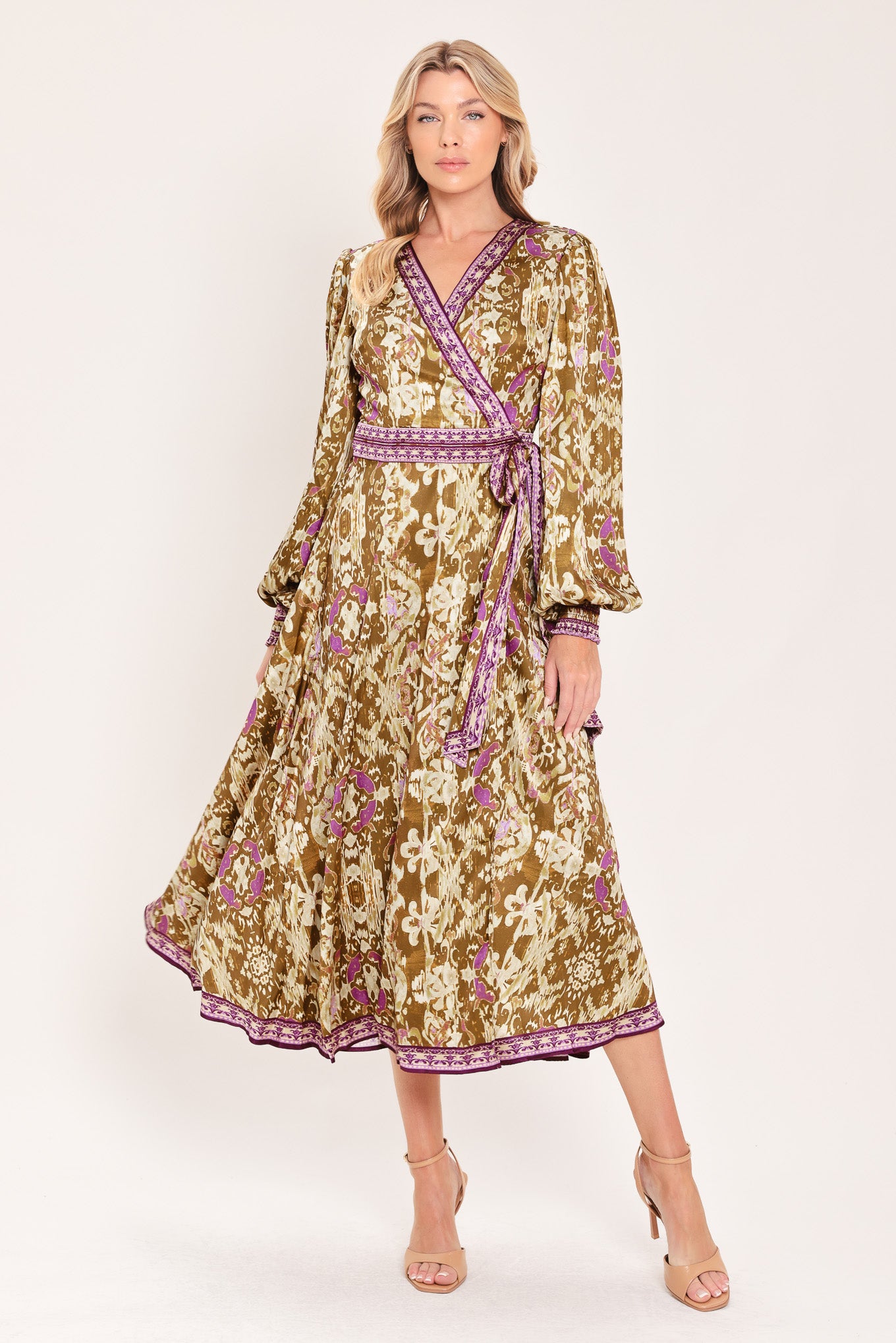 A woman models a long-sleeved midi wrap dress with a brown, beige, and purple floral pattern. The dress features a matching purple patterned belt and hem | Flying Tomato